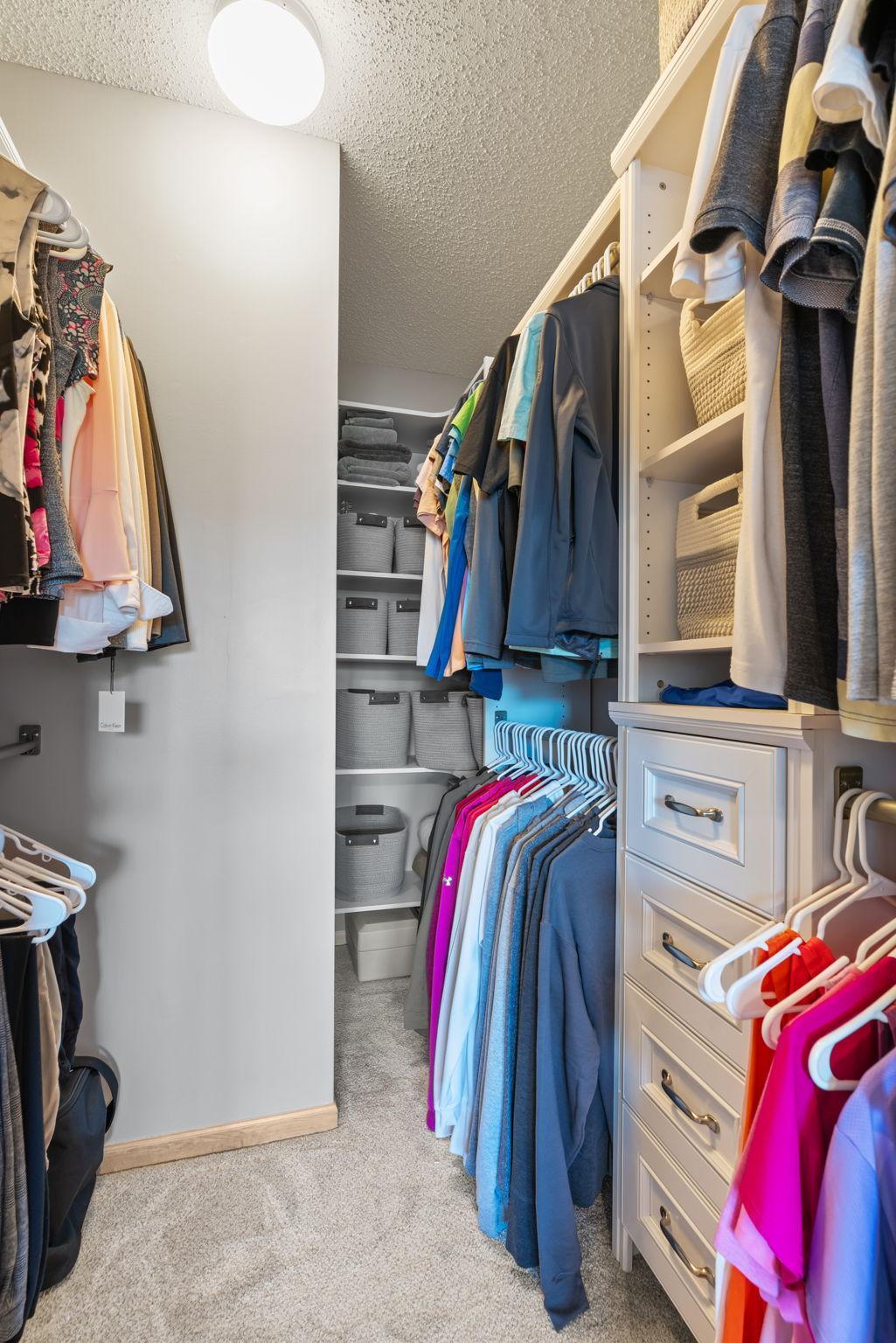 Walk-in closet with built-in shelves, drawers, storage baskets, and neatly hung clothing.