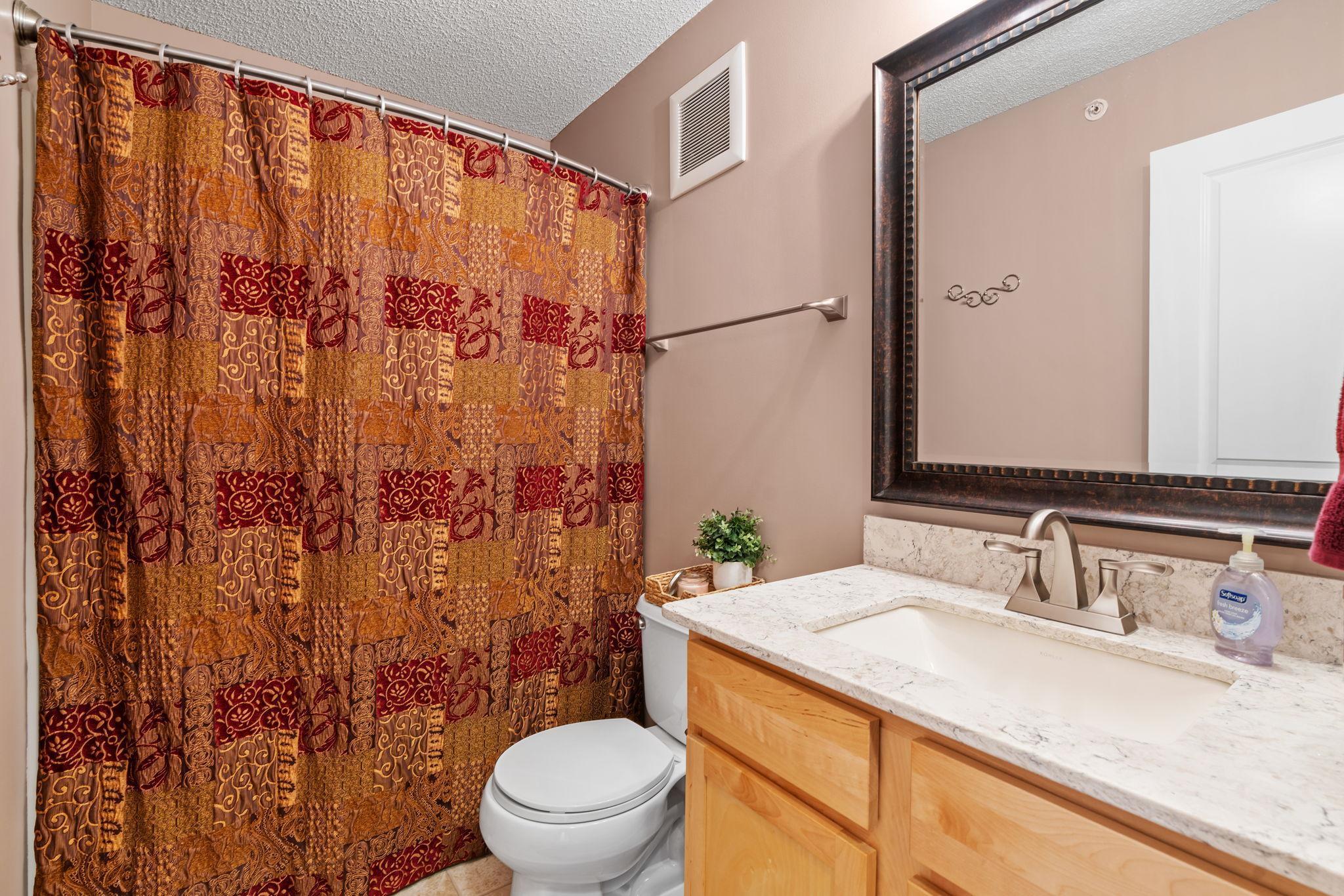 Bathroom with a patterned shower curtain, light wood vanity, marble-look counter, and large mirror.