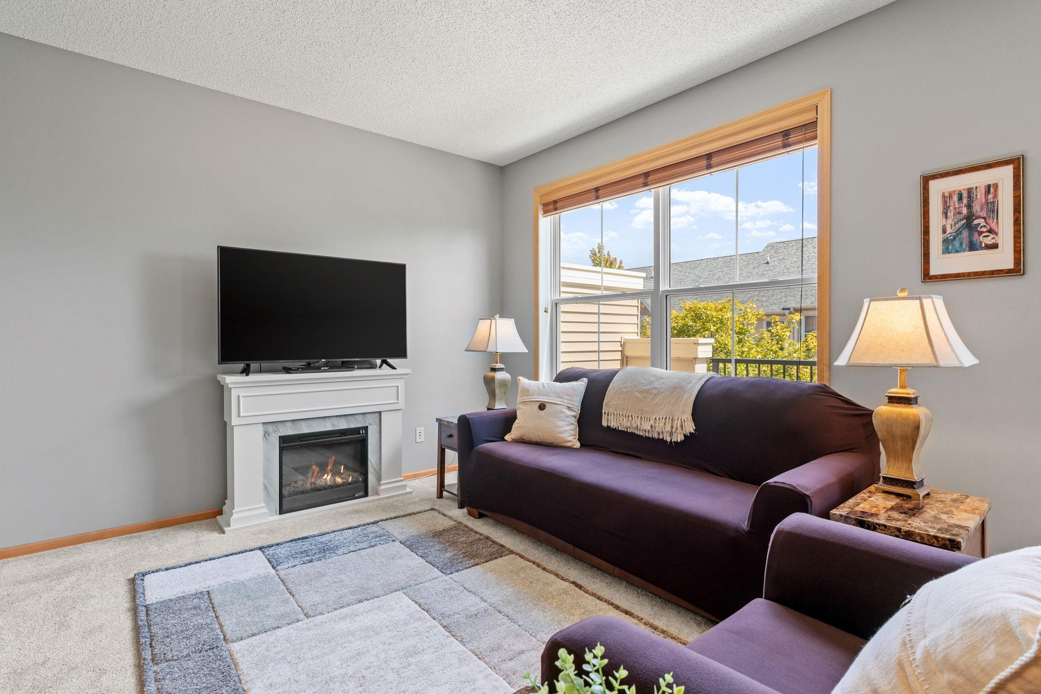 Living room with a dark purple sofa, white fireplace, and large wood-trimmed window.