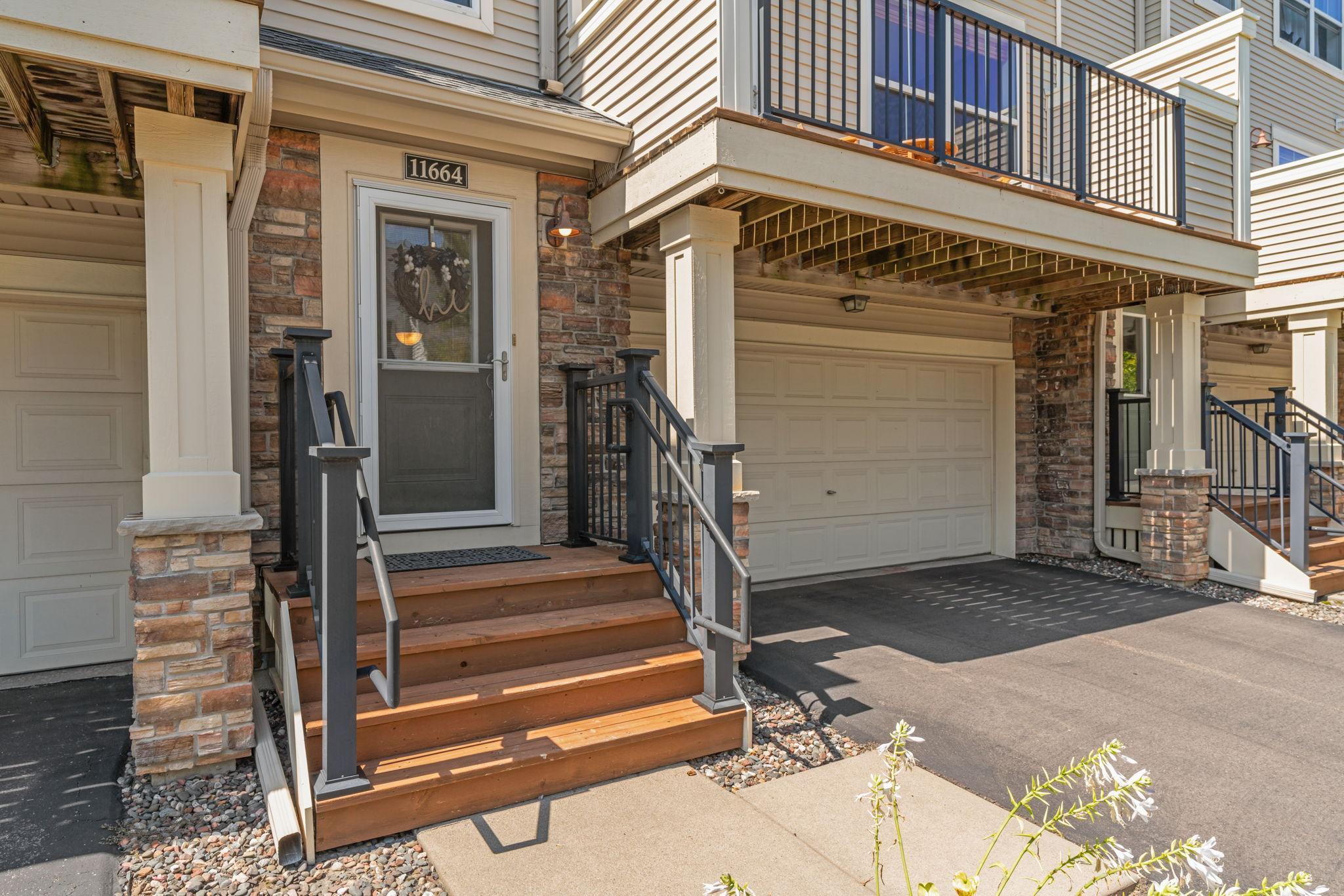 Condominium entrance with wooden steps, stone accents, and an attached garage.