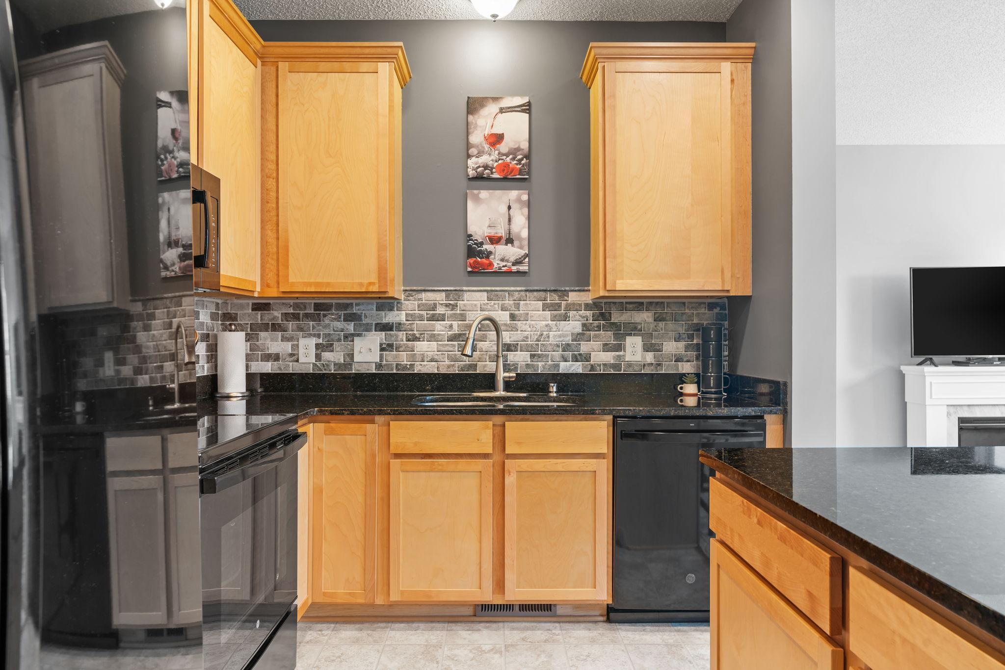 Condo kitchen with honey-toned cabinets, a mosaic backsplash, and black granite counters.