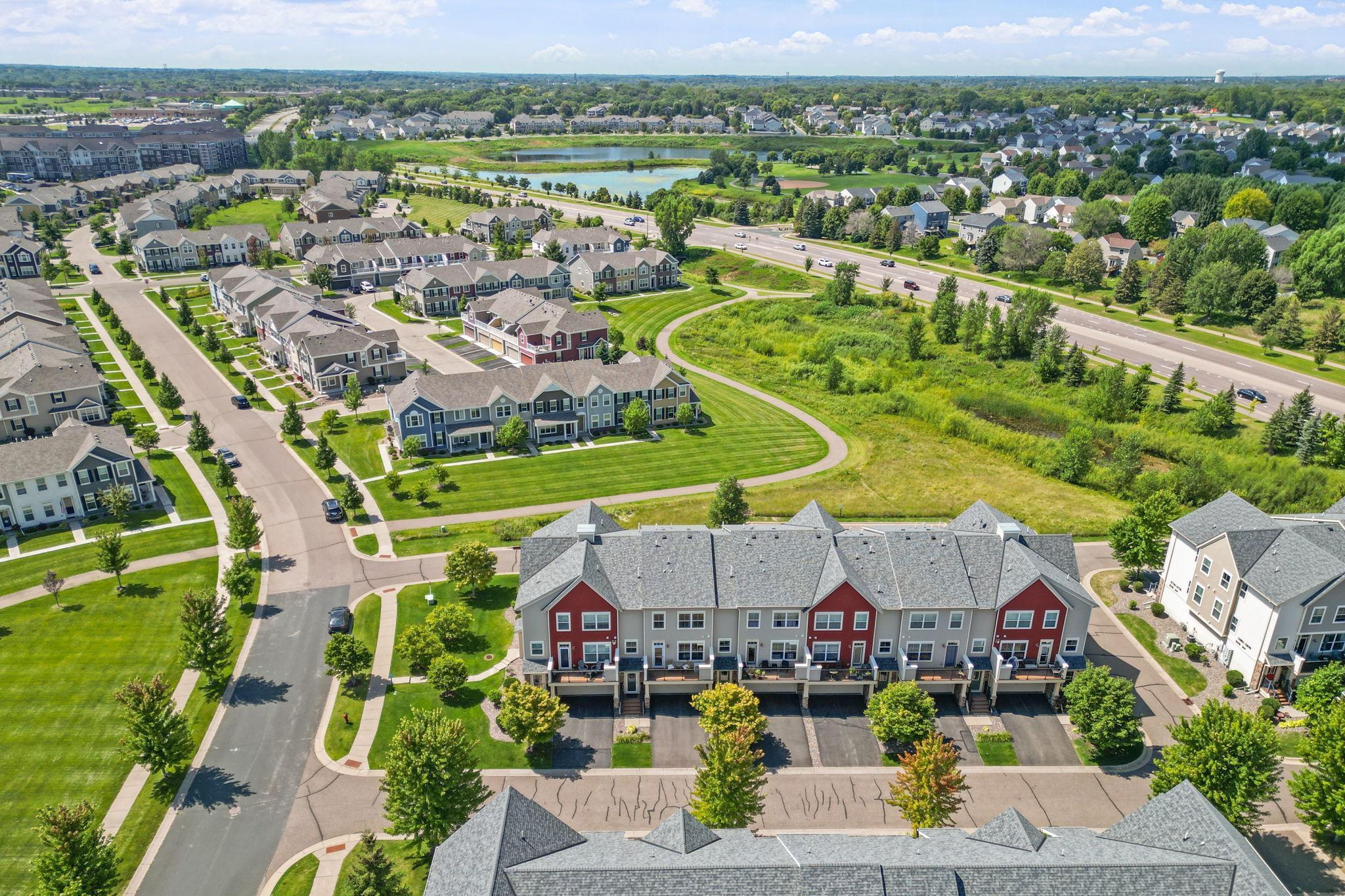 Aerial view of attached townhomes beside landscaped paths, ponds, and a divided road.