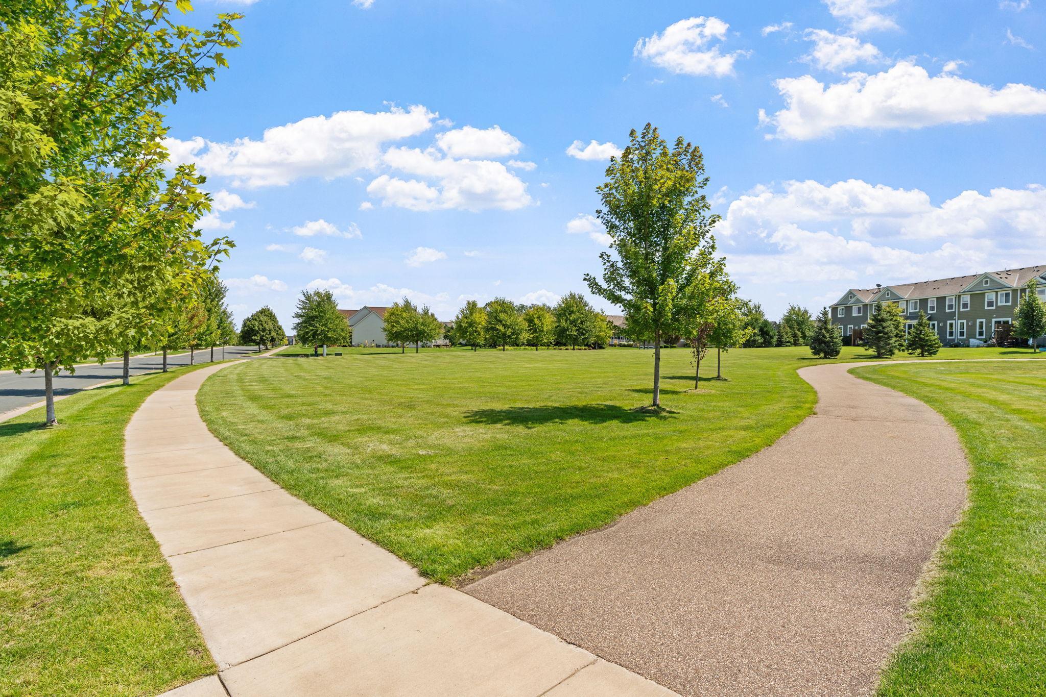 Community grounds with a wide lawn, mature trees, and two curving pedestrian paths.