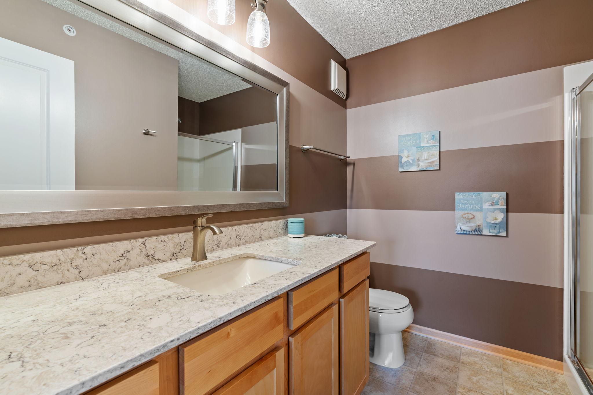 Bathroom with granite vanity, wood cabinets, large mirror, and brown striped walls.