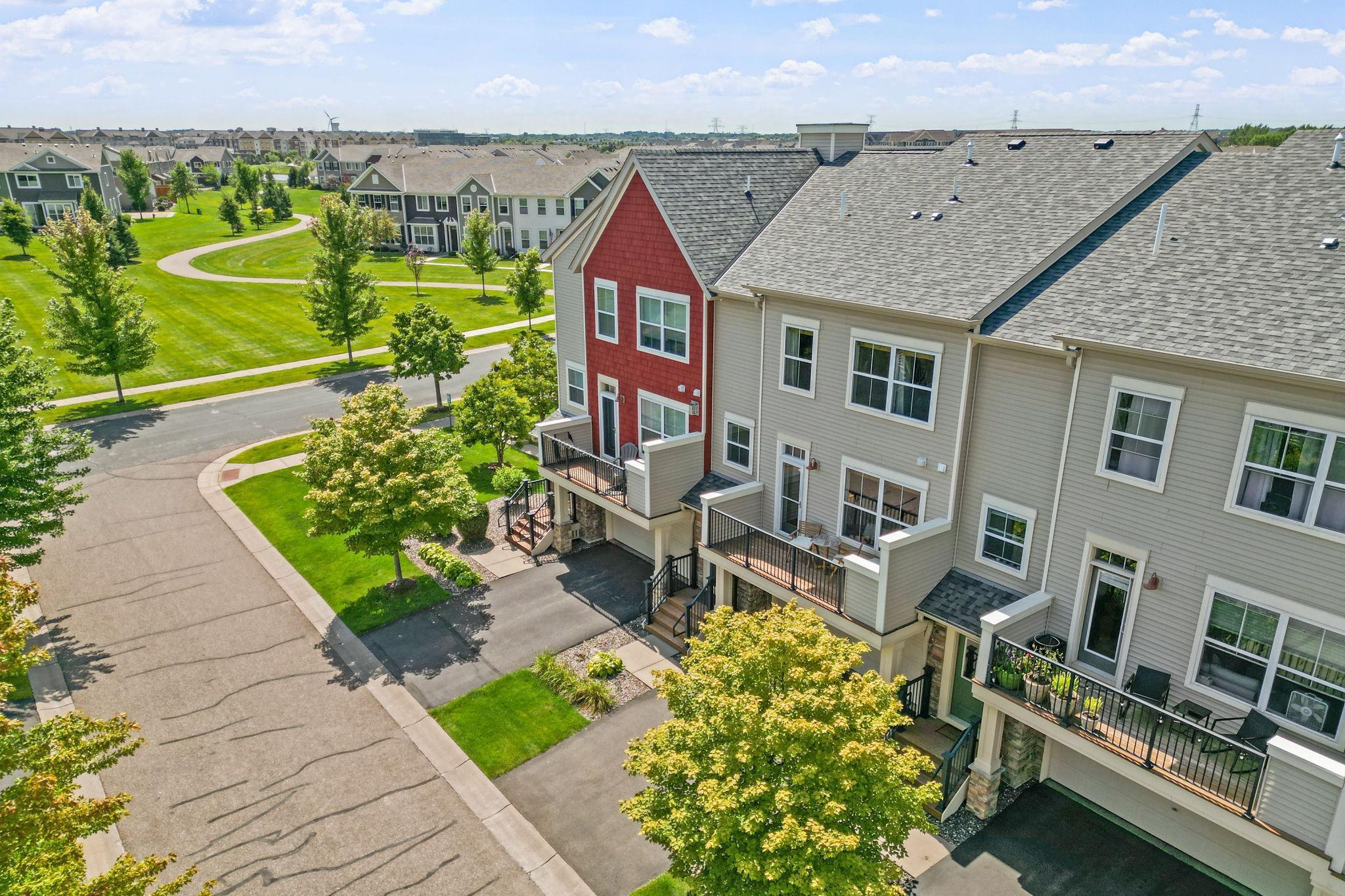 Attached townhomes with raised balconies beside landscaped lawns and a curving community path.