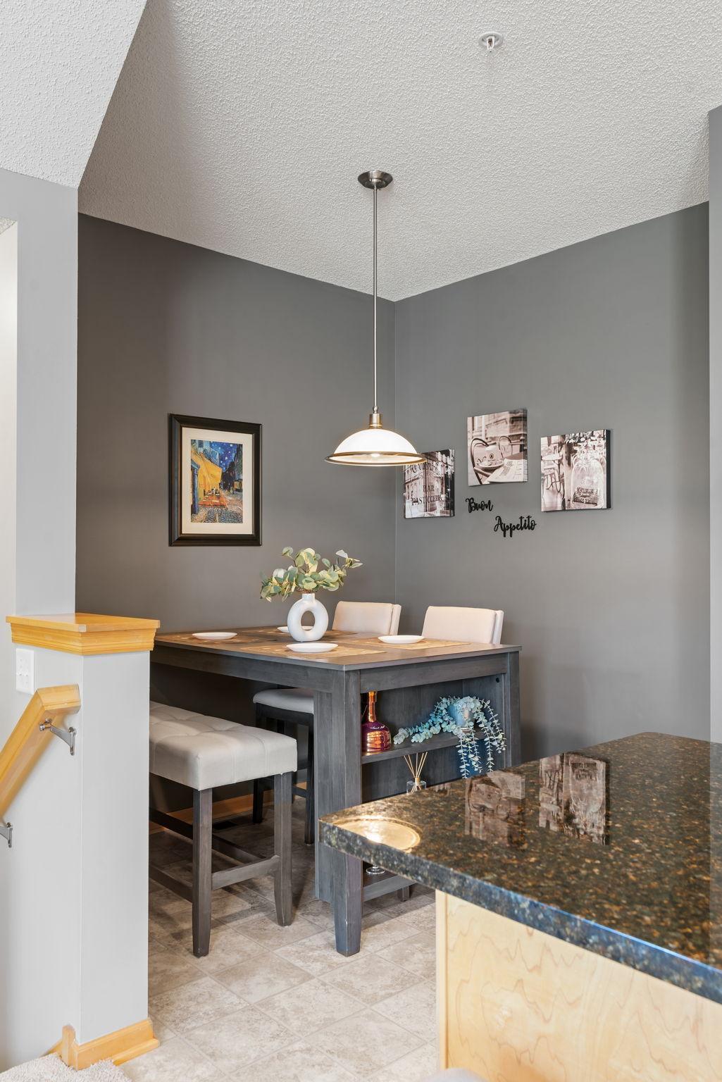 Dining area with a dark gray table, upholstered chairs, pendant light, and “Buon Appetito” wall decor.