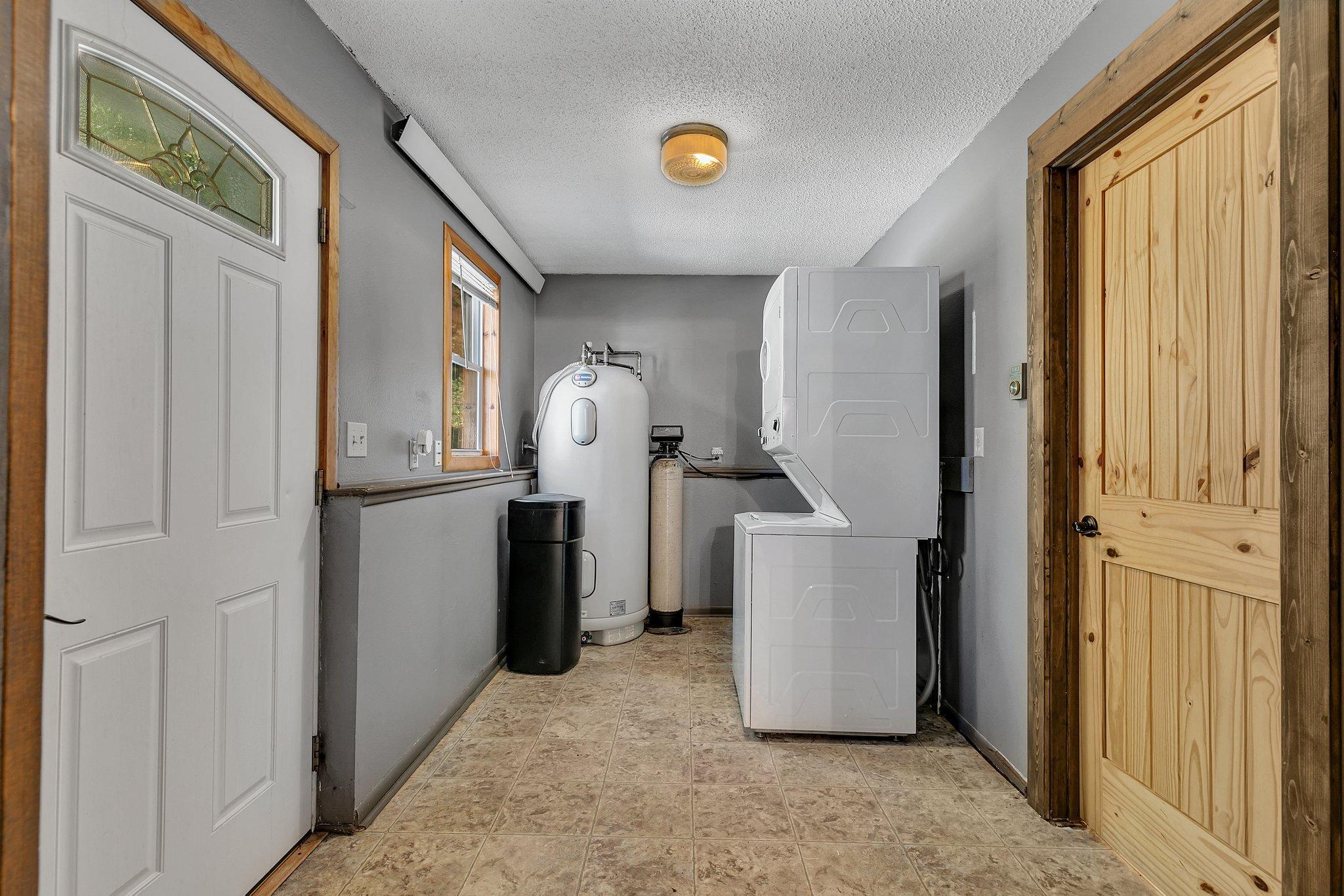 Laundry room with stacked washer and dryer, water heater, and water softener.