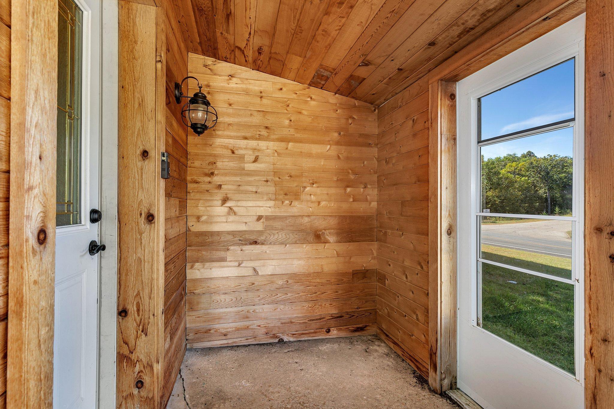 Wood-paneled entry vestibule with a concrete floor, glass doors, and a black wall lantern.
