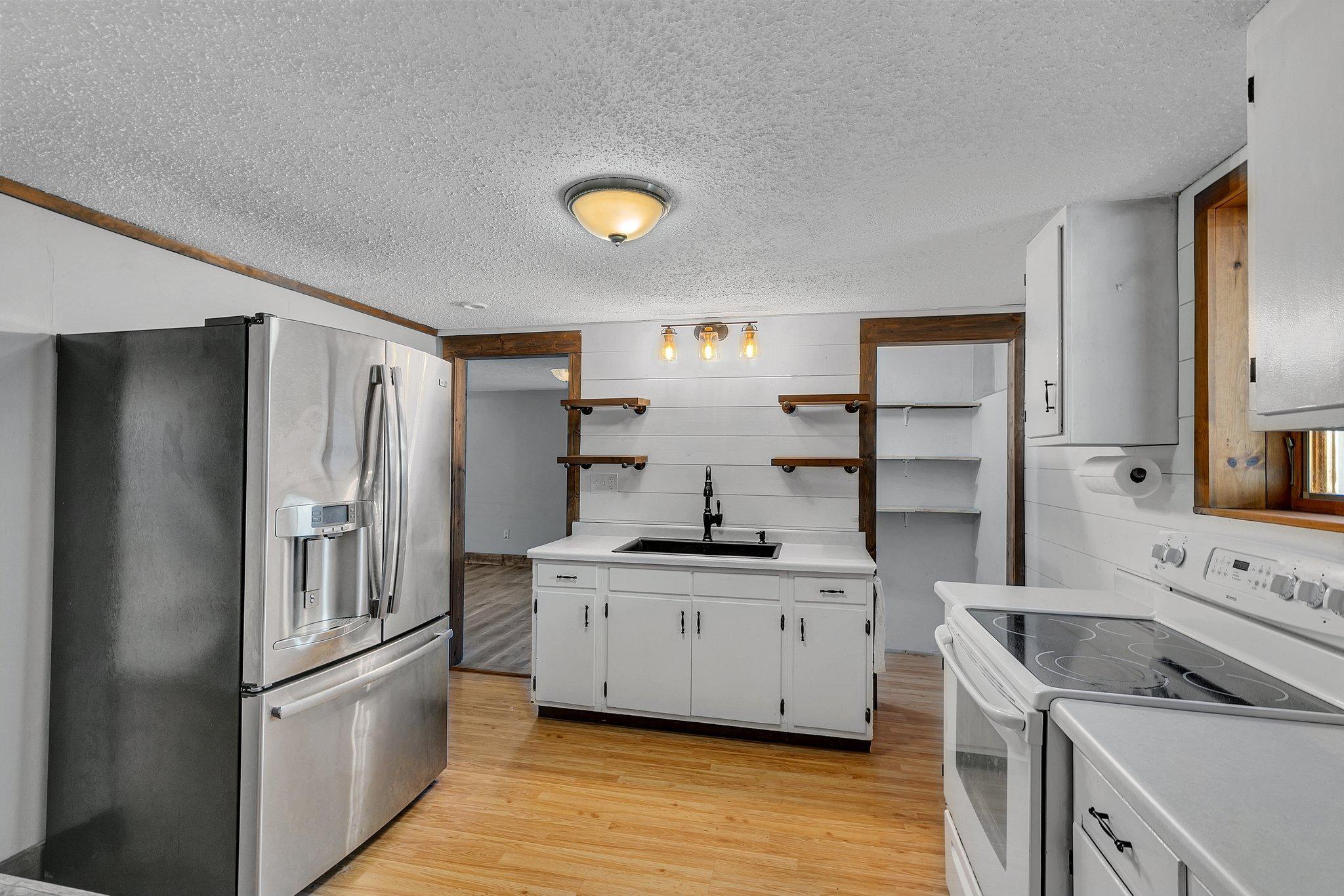 Kitchen with central sink, white cabinets, stainless-steel refrigerator, and electric range.