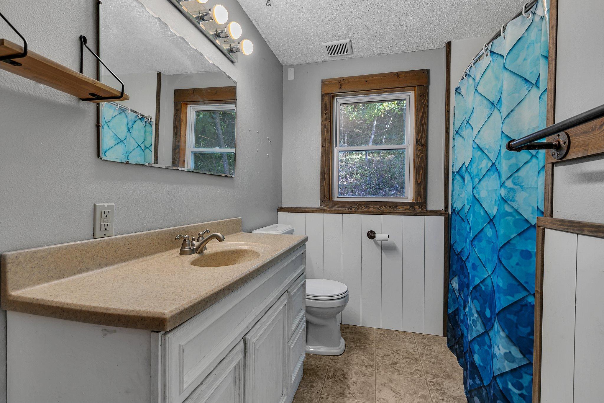 Bathroom with a tan vanity countertop, blue patterned shower curtain, and wood-trimmed window.