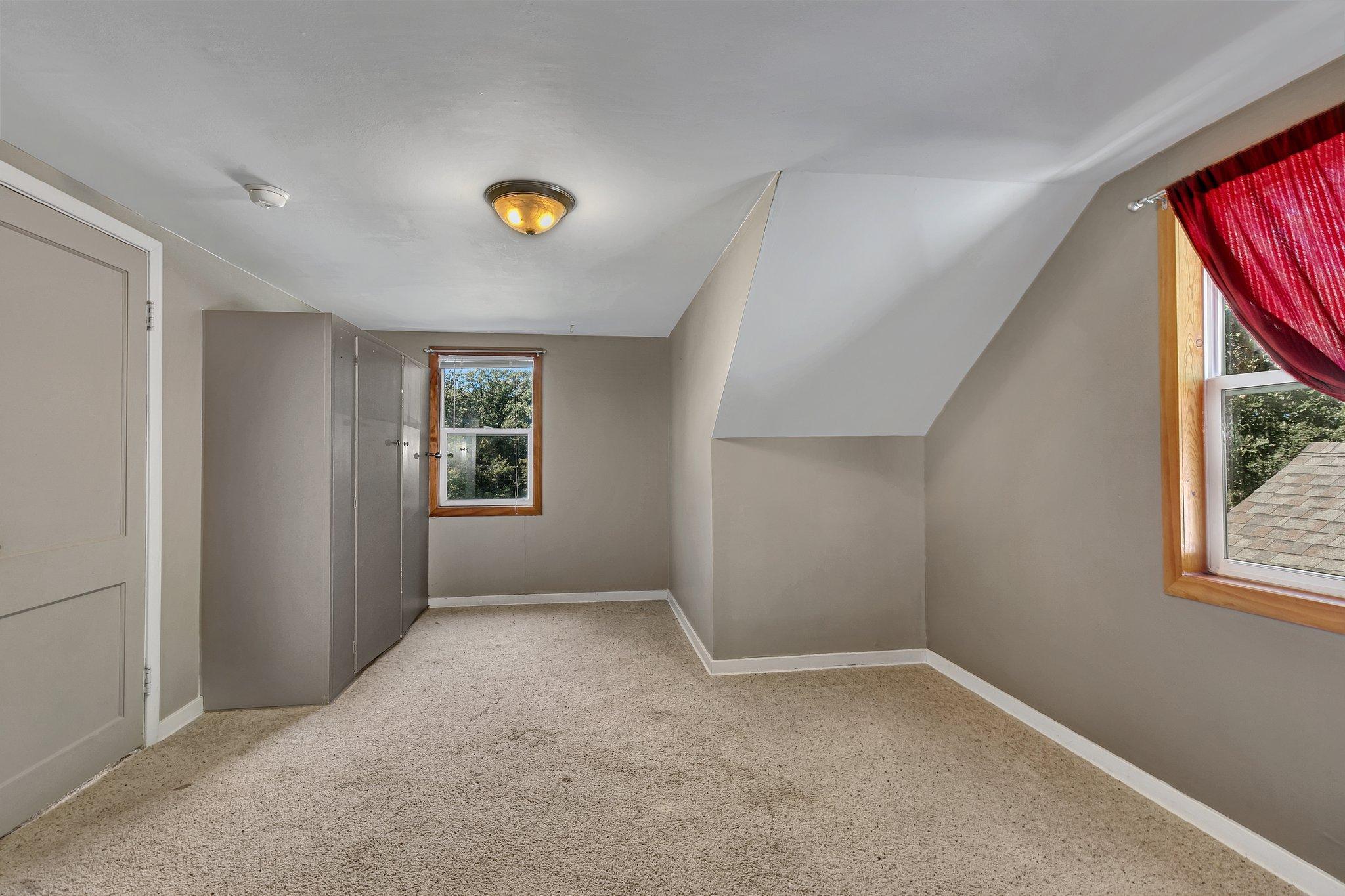 Empty upstairs bedroom with built-in closets, a sloped ceiling, and a red curtain.