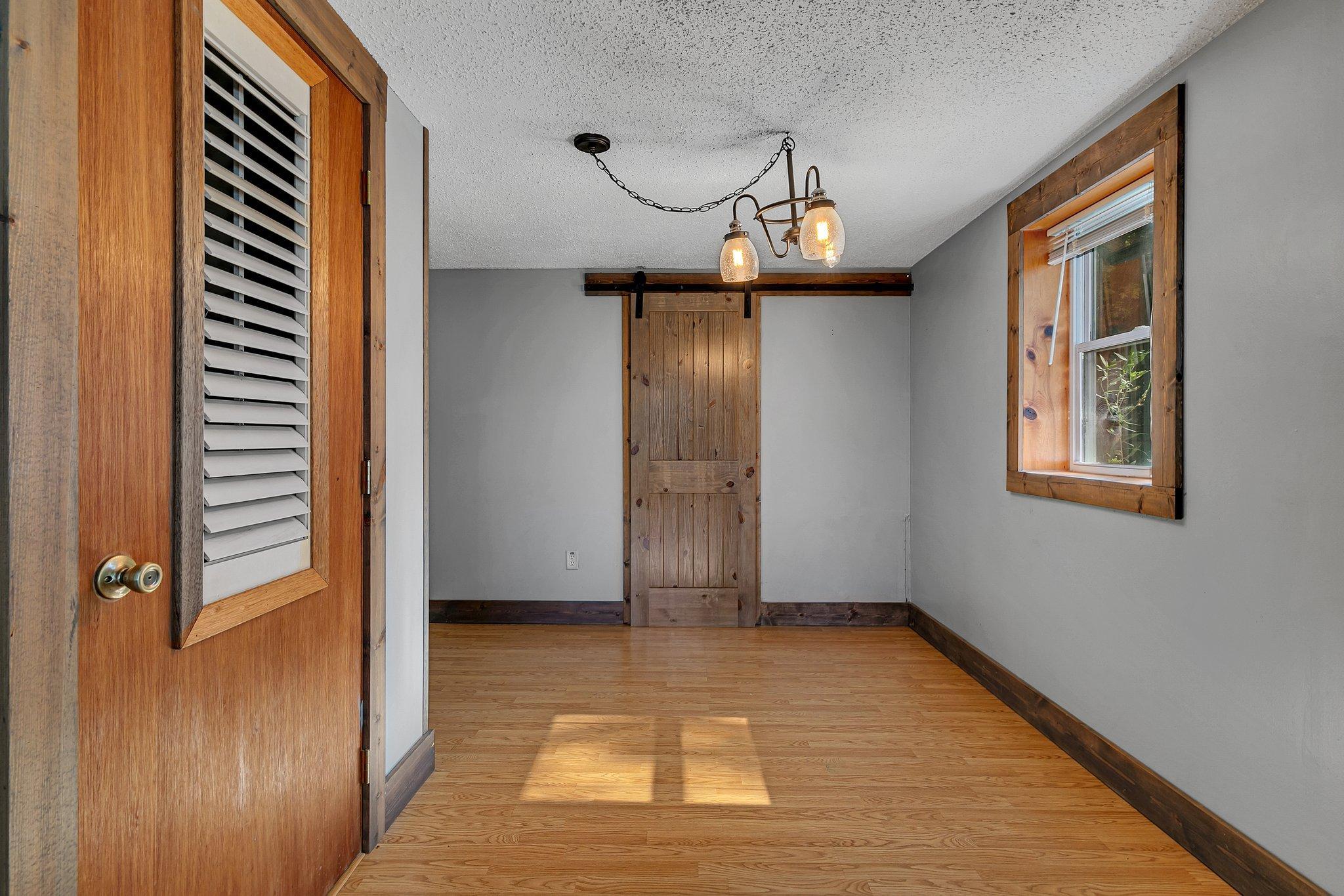 Empty room with hardwood floors, rustic wood trim, and a sliding barn door.