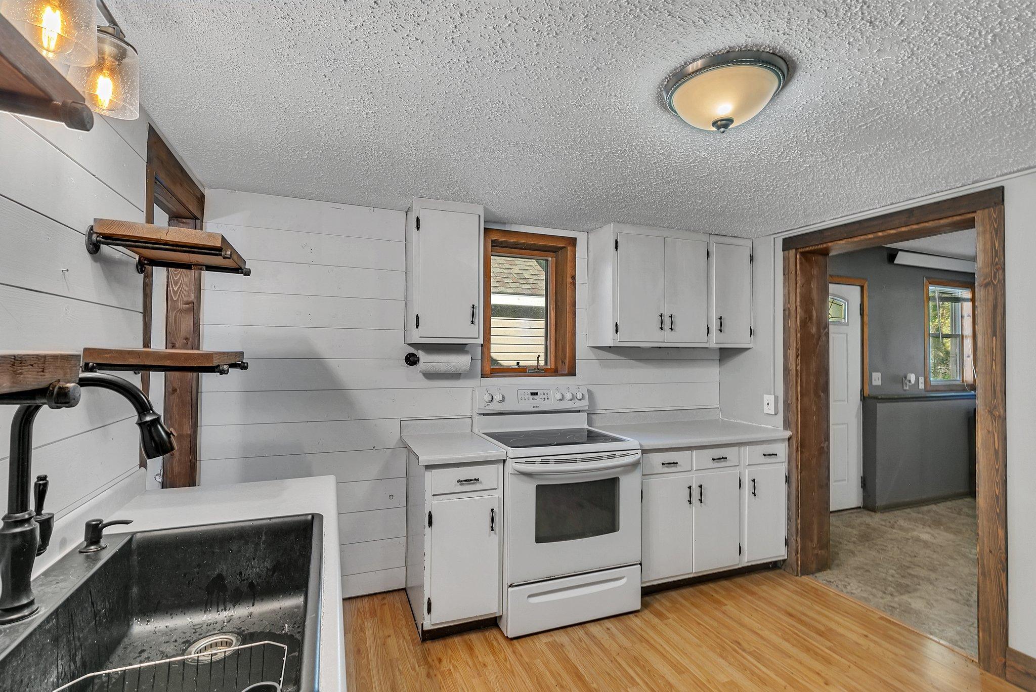 Kitchen with white plank walls, a white electric range, stainless steel sink, and dark wood trim.