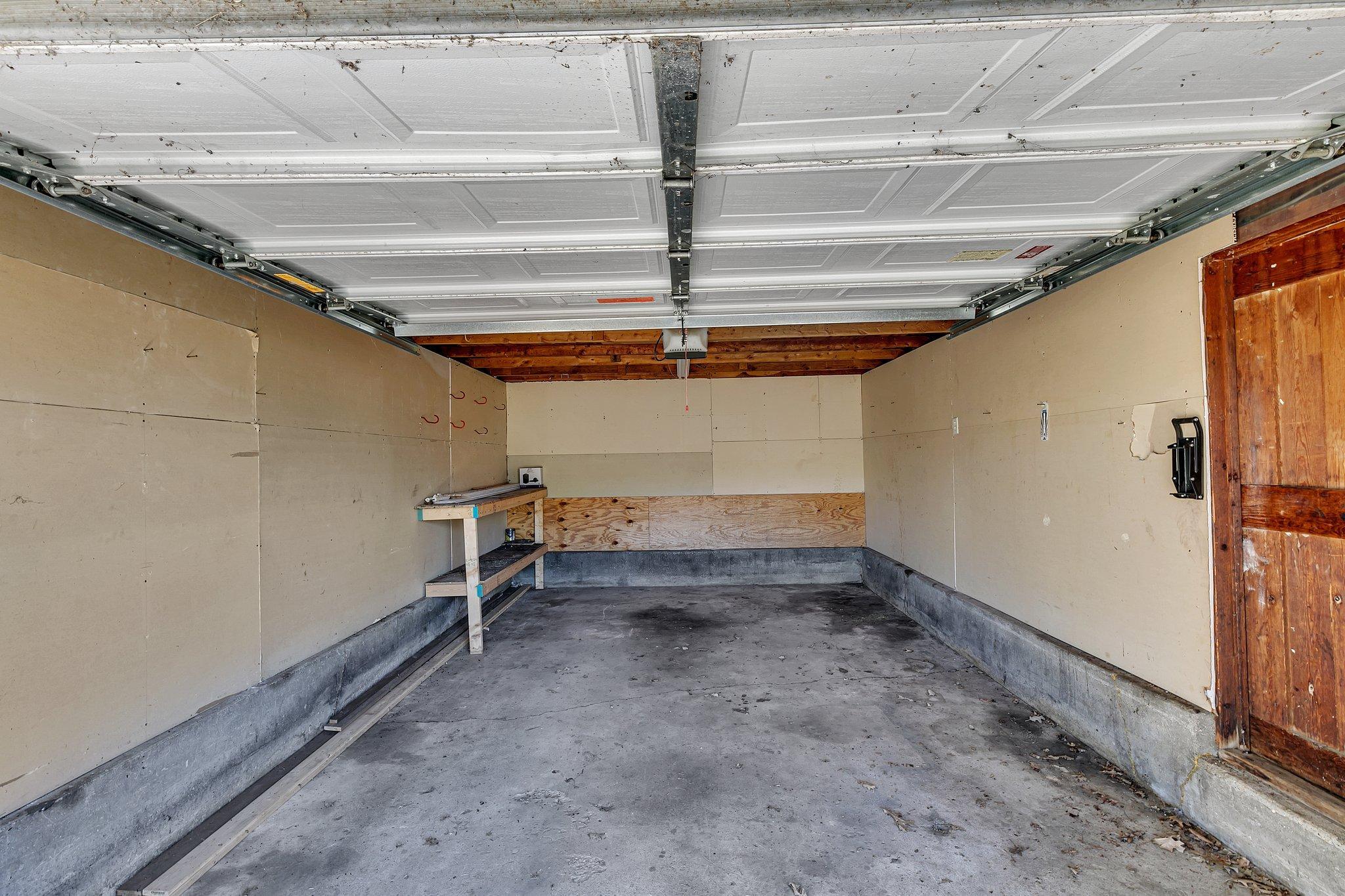 Empty garage with a raised overhead door, concrete floor, workbench, and wooden side door.