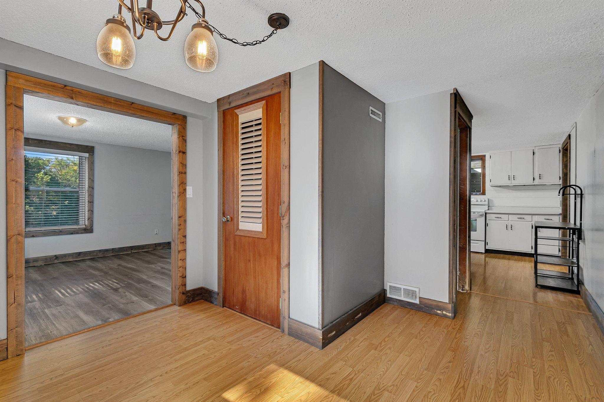 Entry hall with rustic wood trim, a louvered door, and views into an adjoining room and kitchen.
