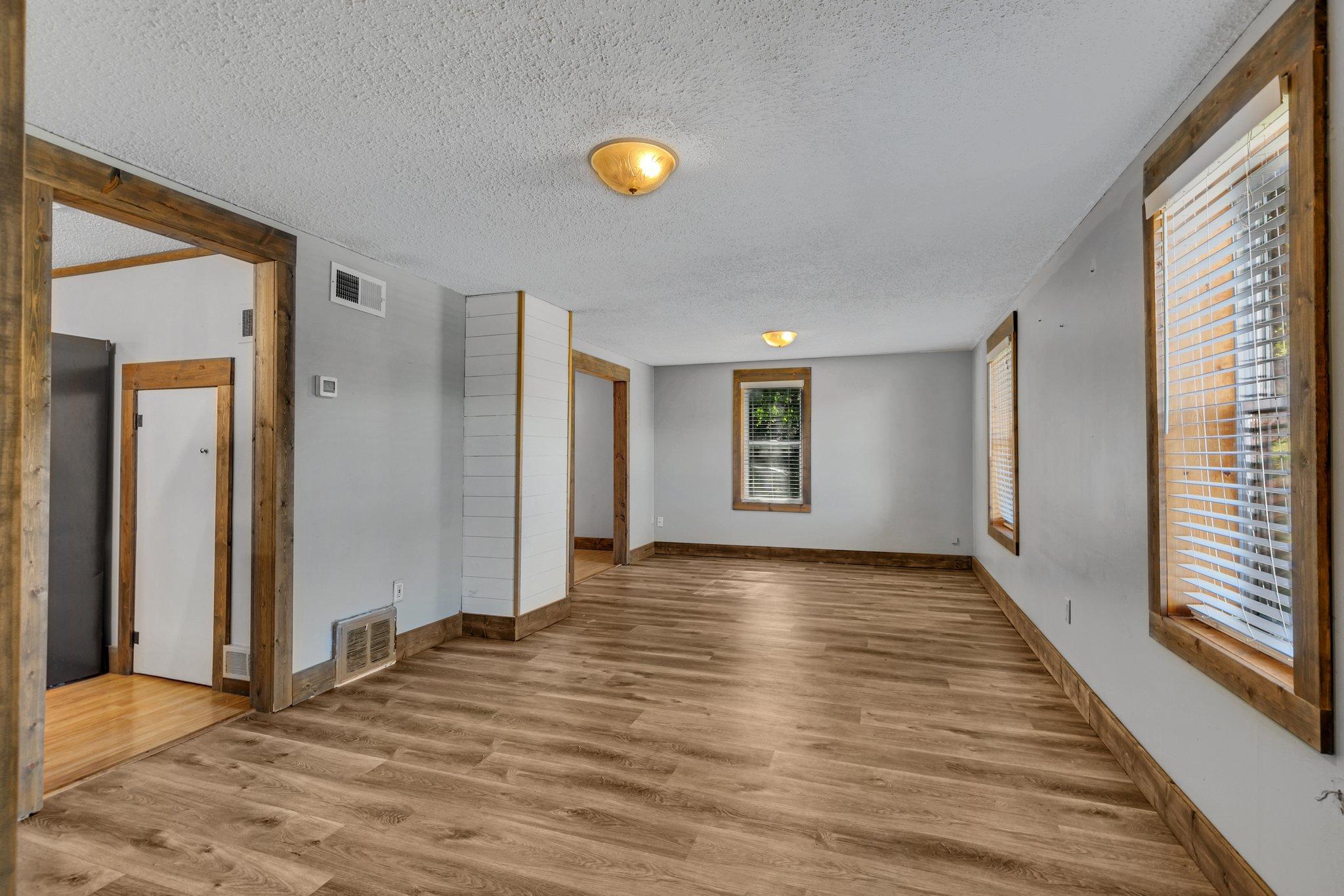 Empty living room with wood-look floors, rustic wood trim, and windows with blinds.