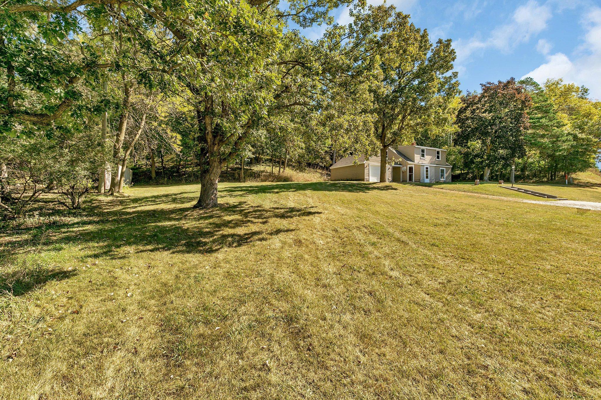 Two-story home and garage set back on a broad lawn beneath mature trees.