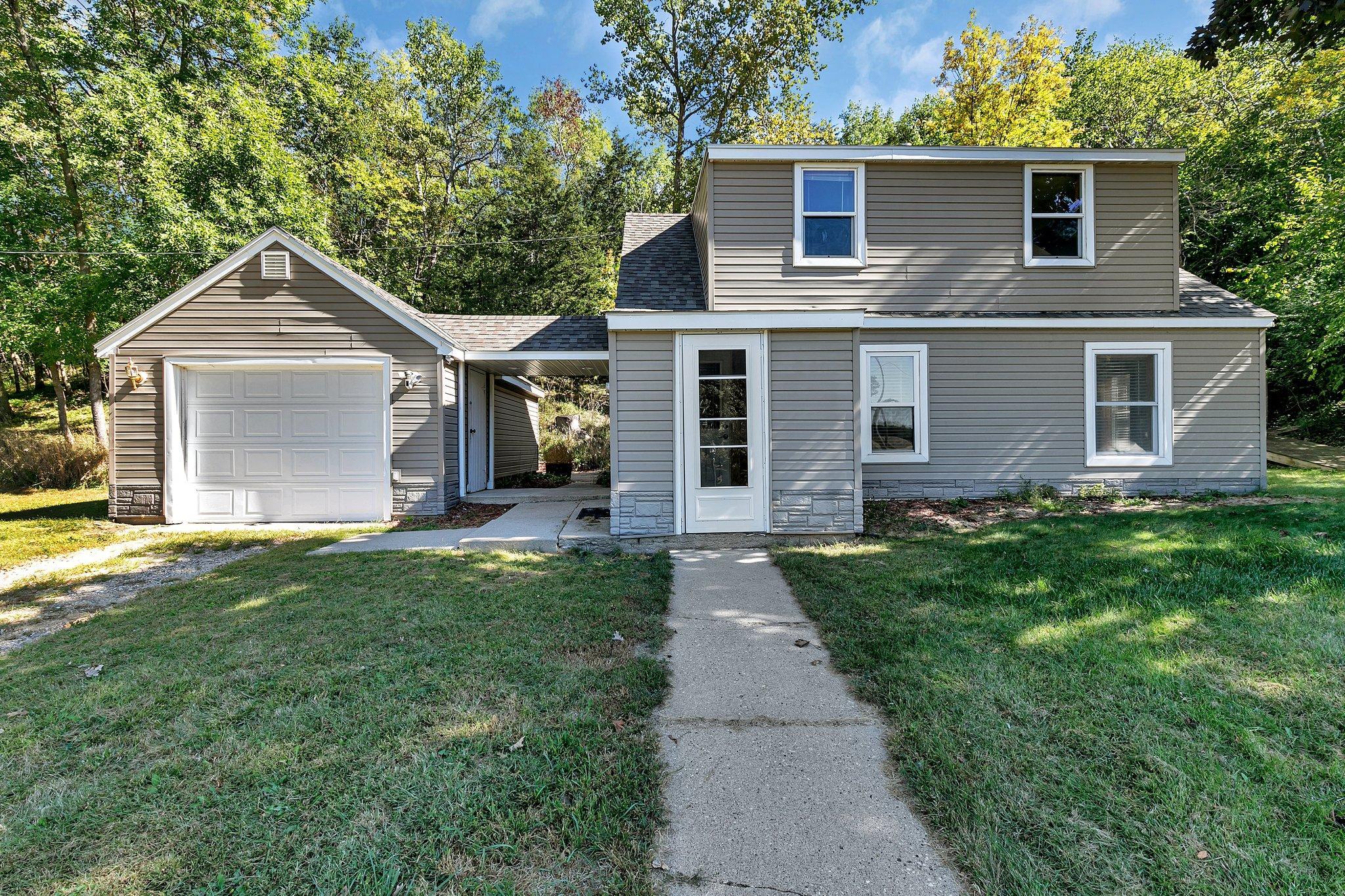 Two-story gray-sided house with a single-car garage, covered passage, and concrete front walkway.