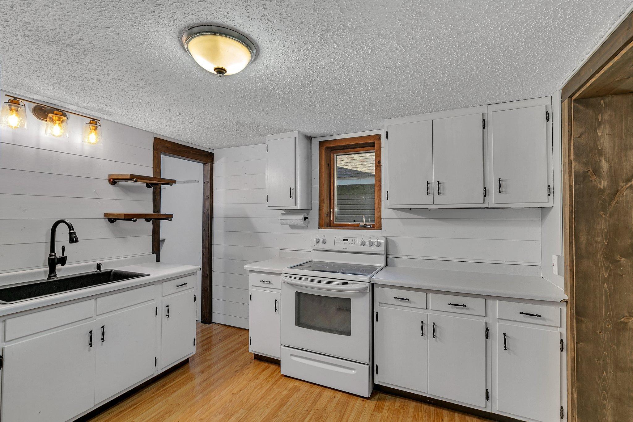 Kitchen with white cabinets, black sink, electric range, and wood-trimmed window.