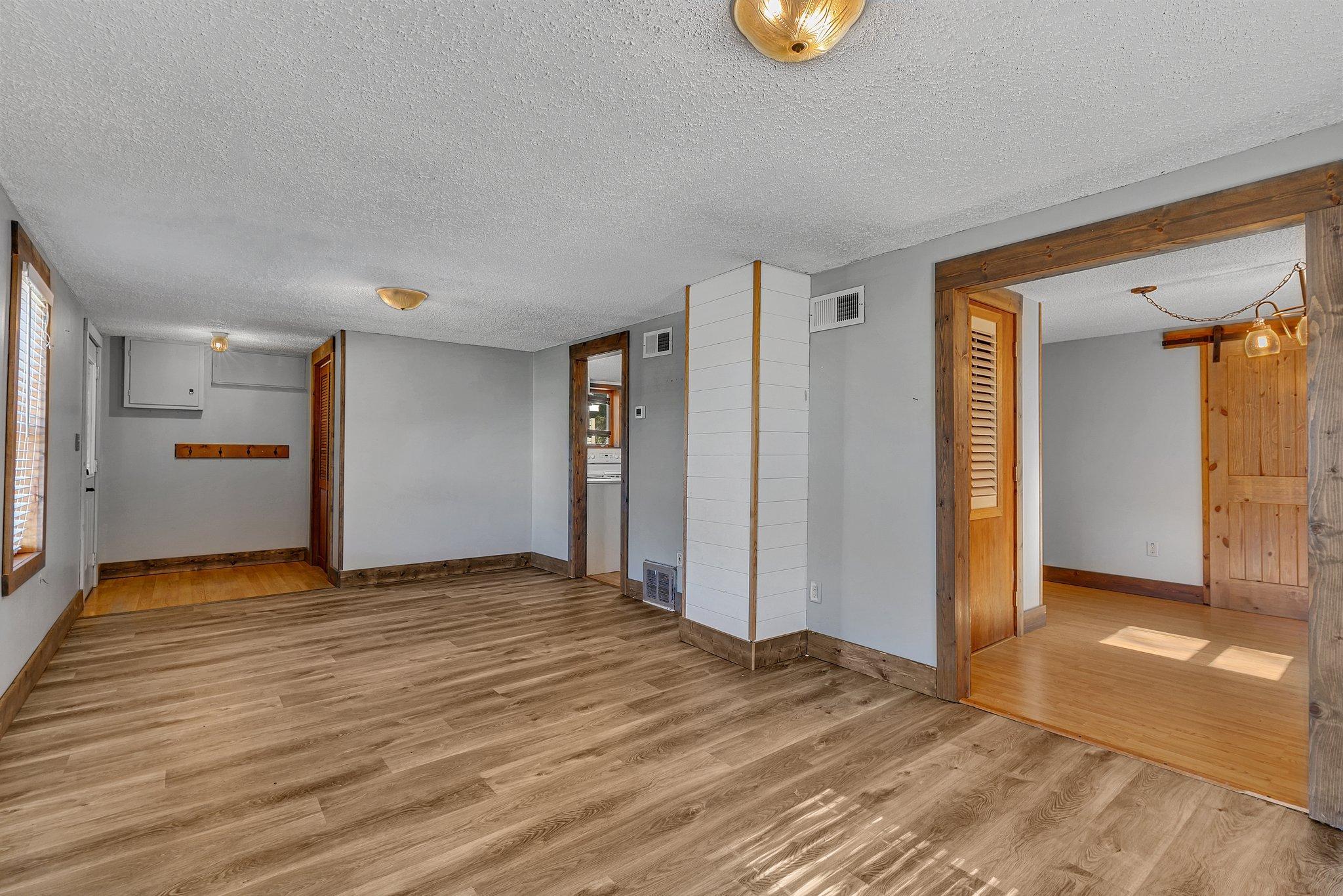 Empty room with wood-look flooring, rustic trim, and an open doorway to a wood-floored room.
