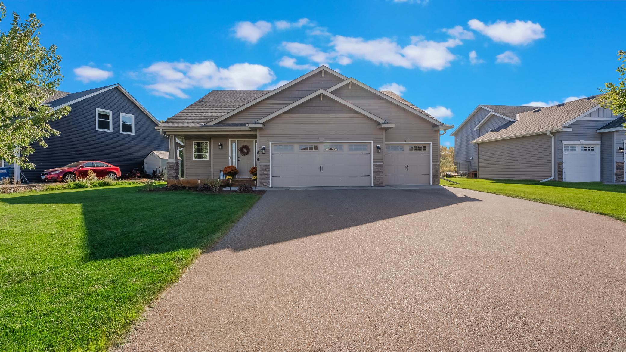 Gray home with a three-car garage, covered entry, and wide driveway in bright sunshine.