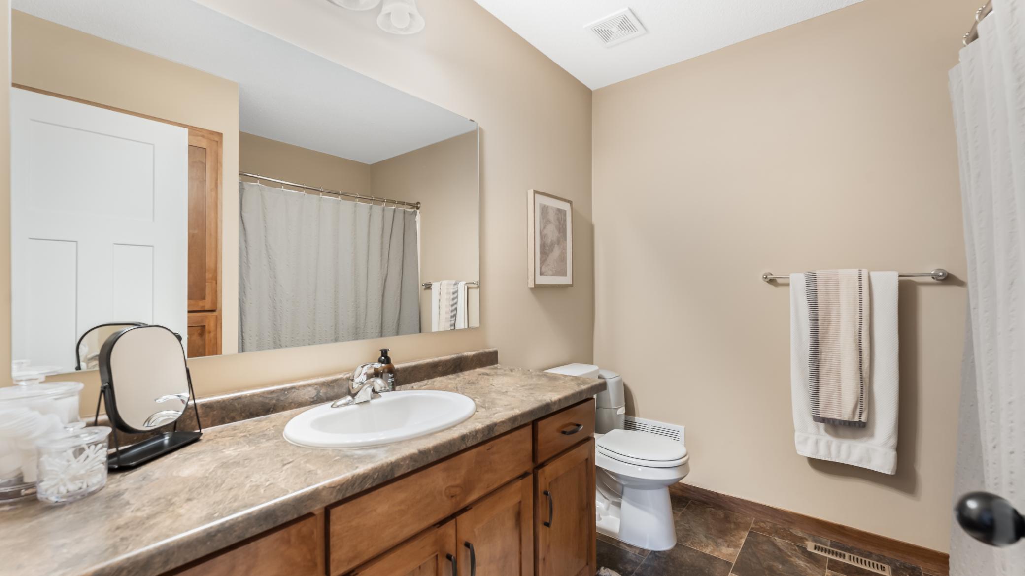 Bathroom with a long wood vanity, stone countertop, large mirror, and toilet.