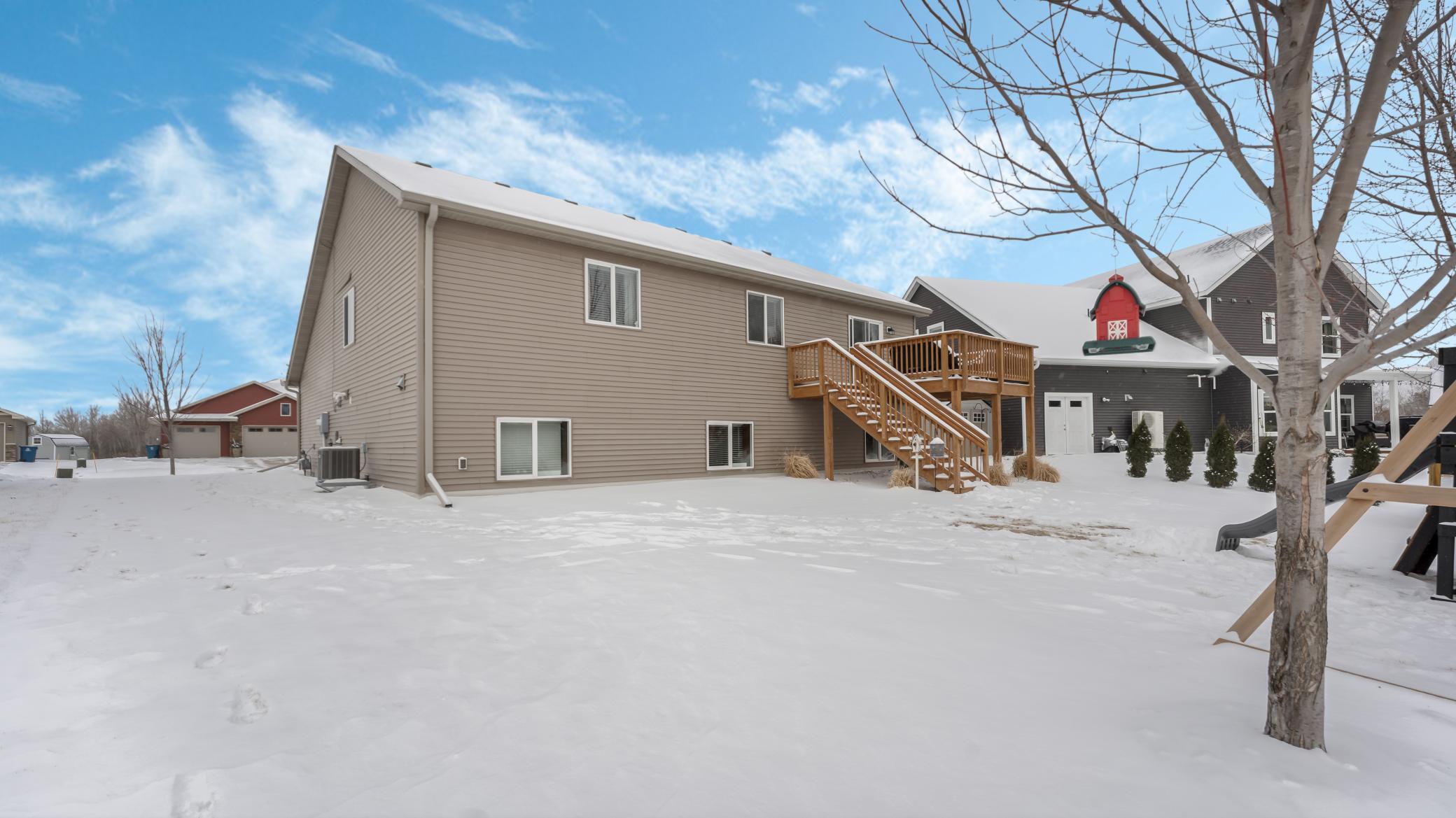 Rear of a taupe-sided house with a raised wooden deck and stairs in a snowy backyard.