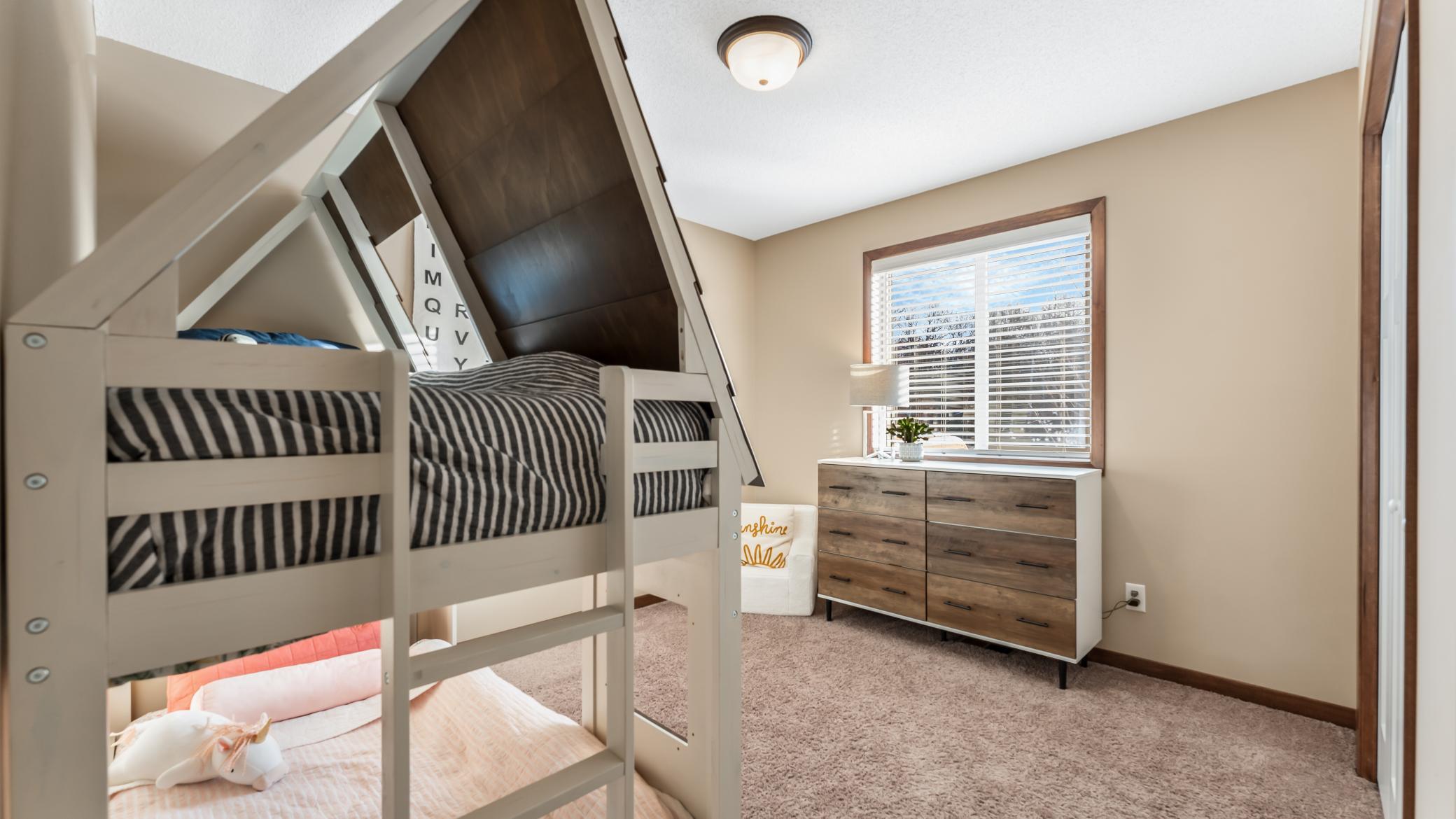 Bedroom with a white bunk bed, striped bedding, and a wooden dresser beneath a window.