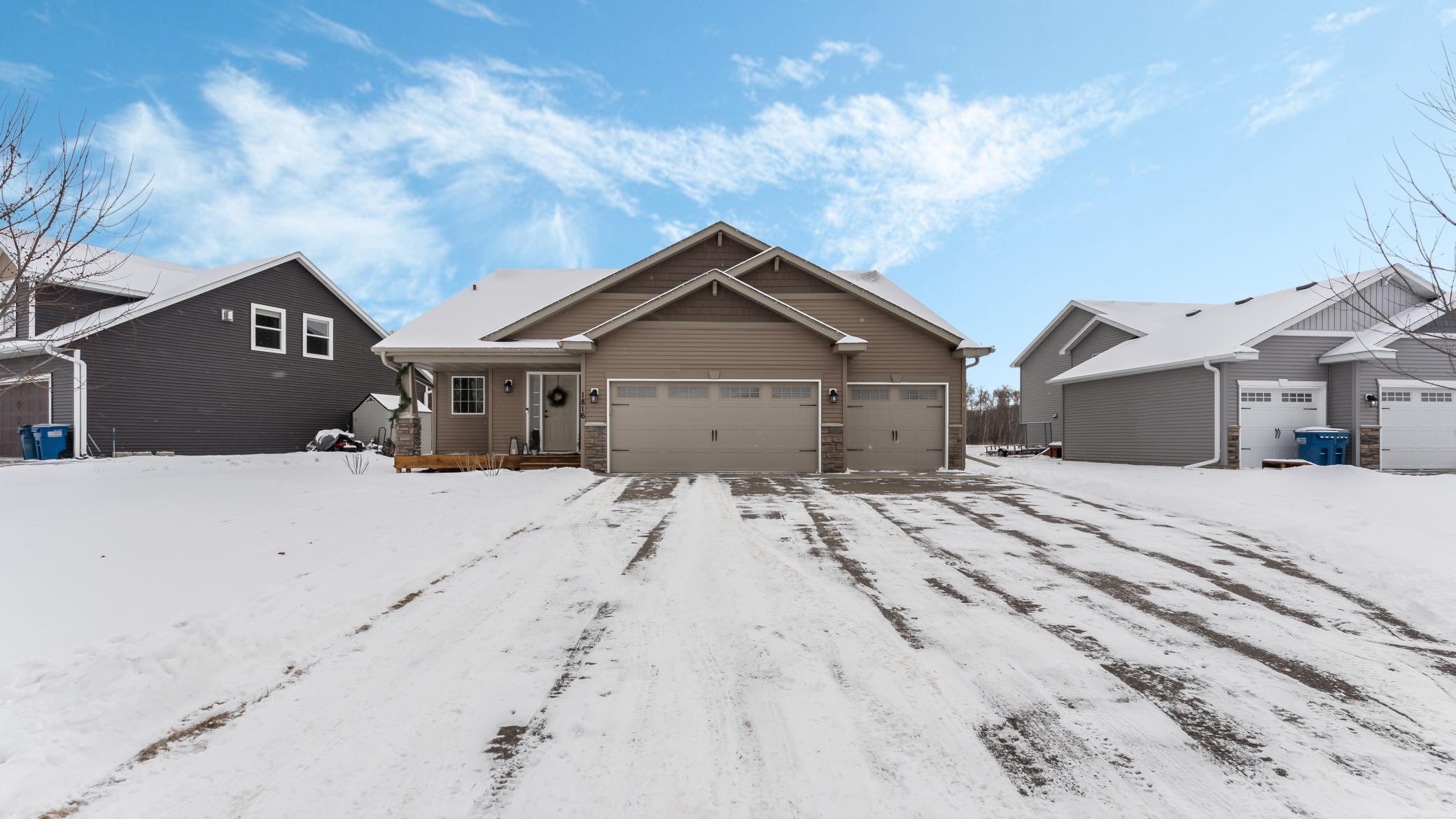 Taupe home with a three-car garage and snow-covered driveway between neighboring houses.