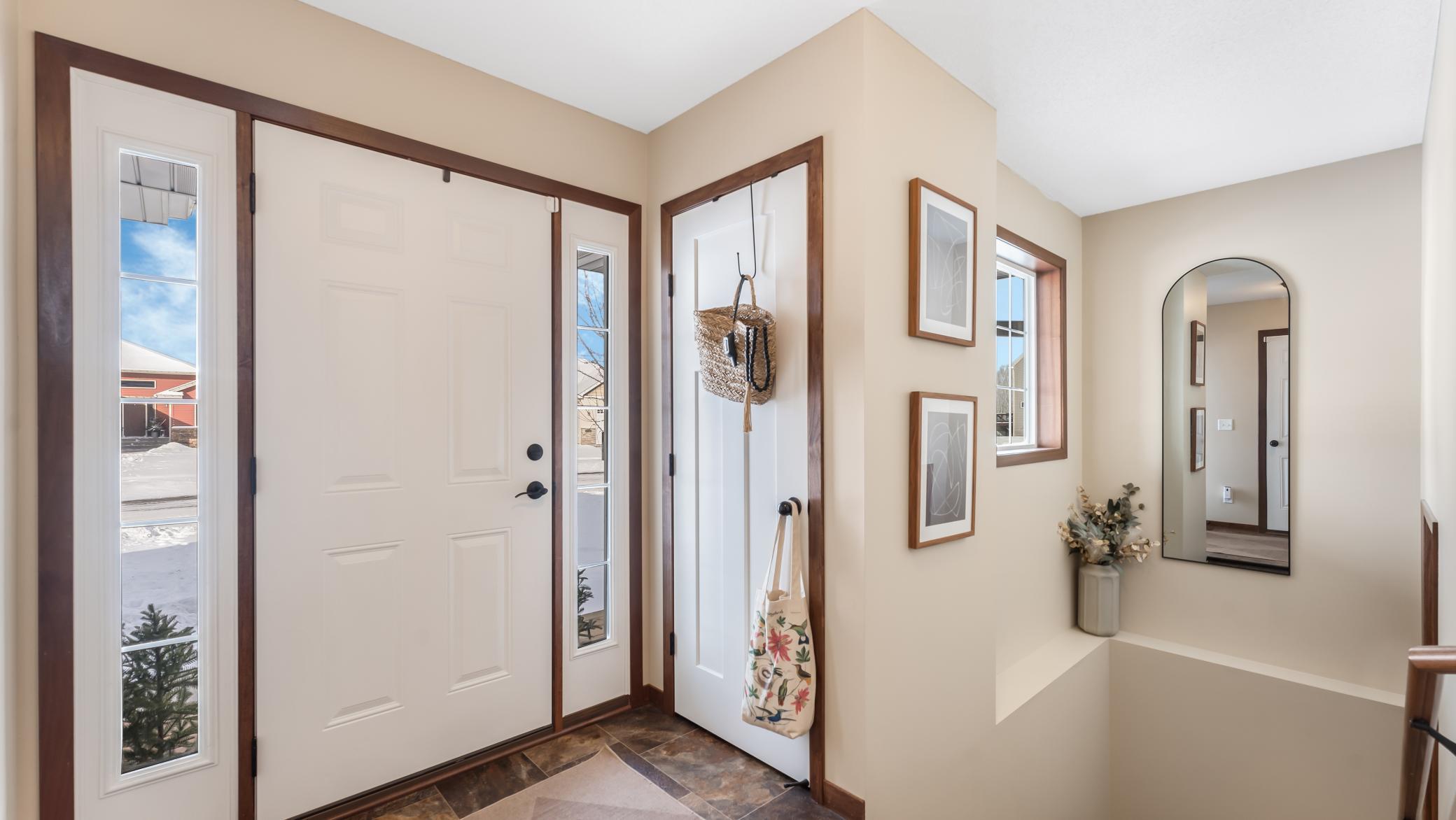 Entryway with white doors, dark wood trim, tiled floor, and an arched mirror.