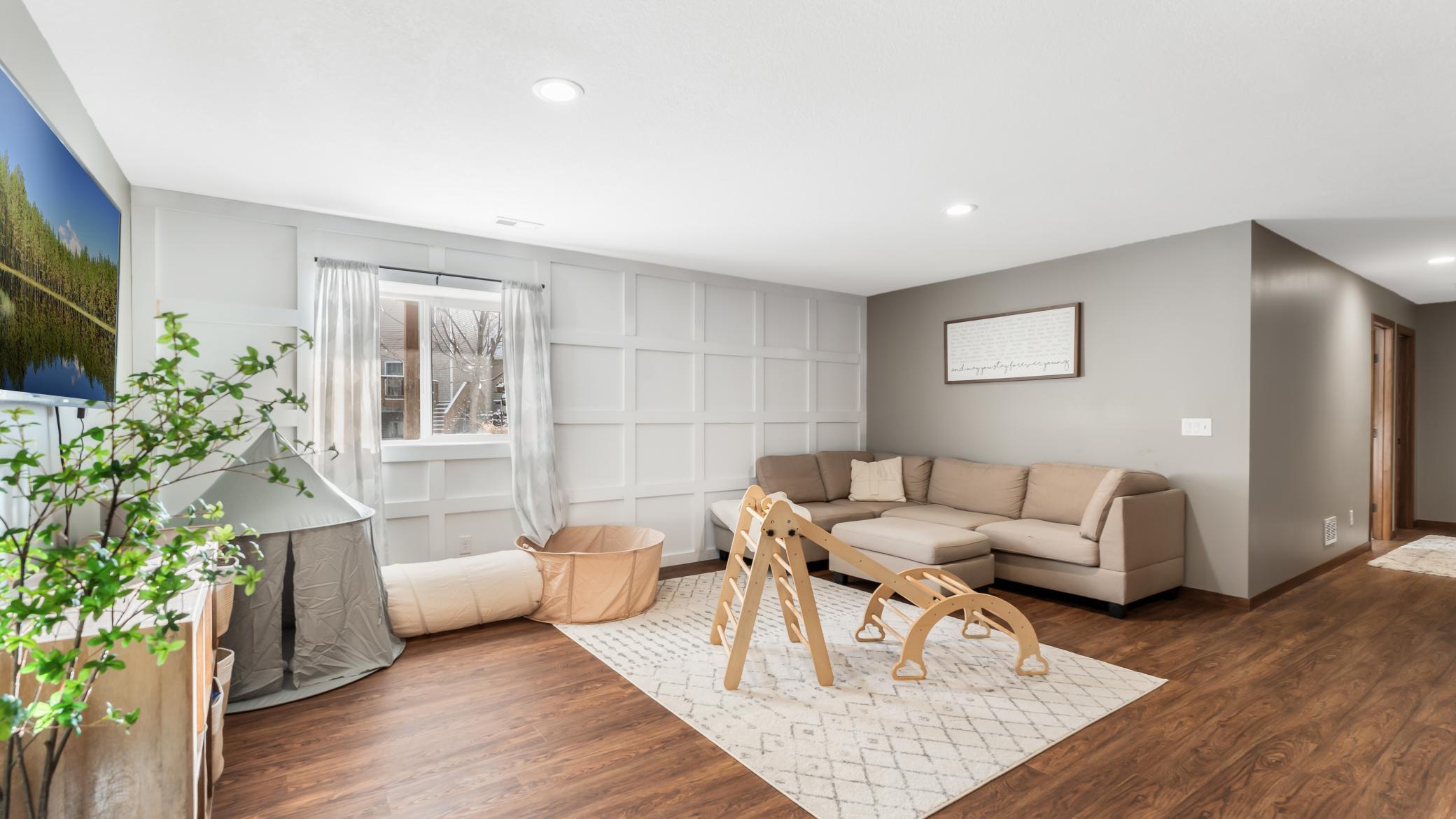 Living room with a taupe sectional, white paneled wall, patterned rug, and wooden play equipment.
