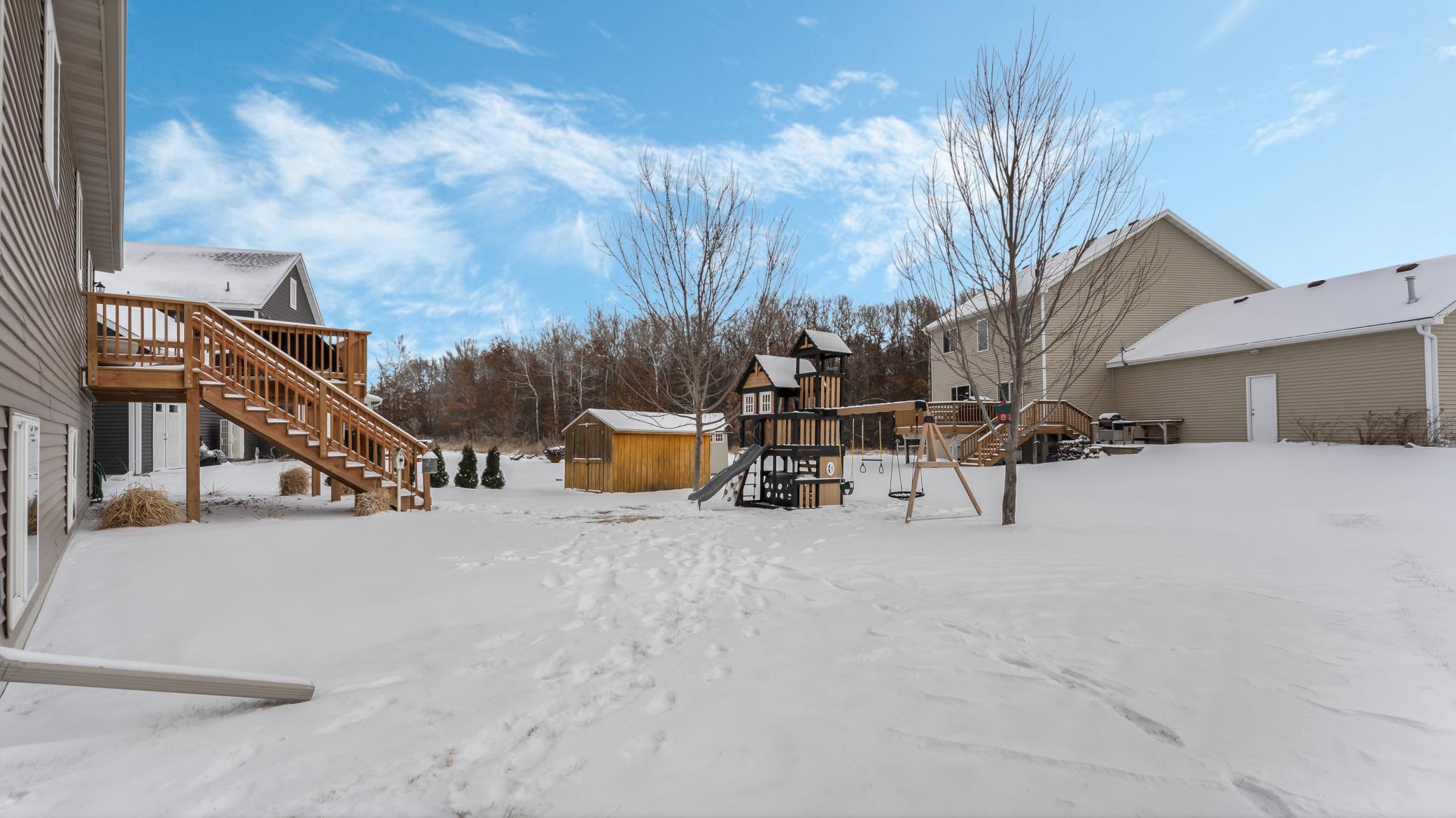 Snow-covered backyard with a raised wooden deck, children’s playset, and storage shed.
