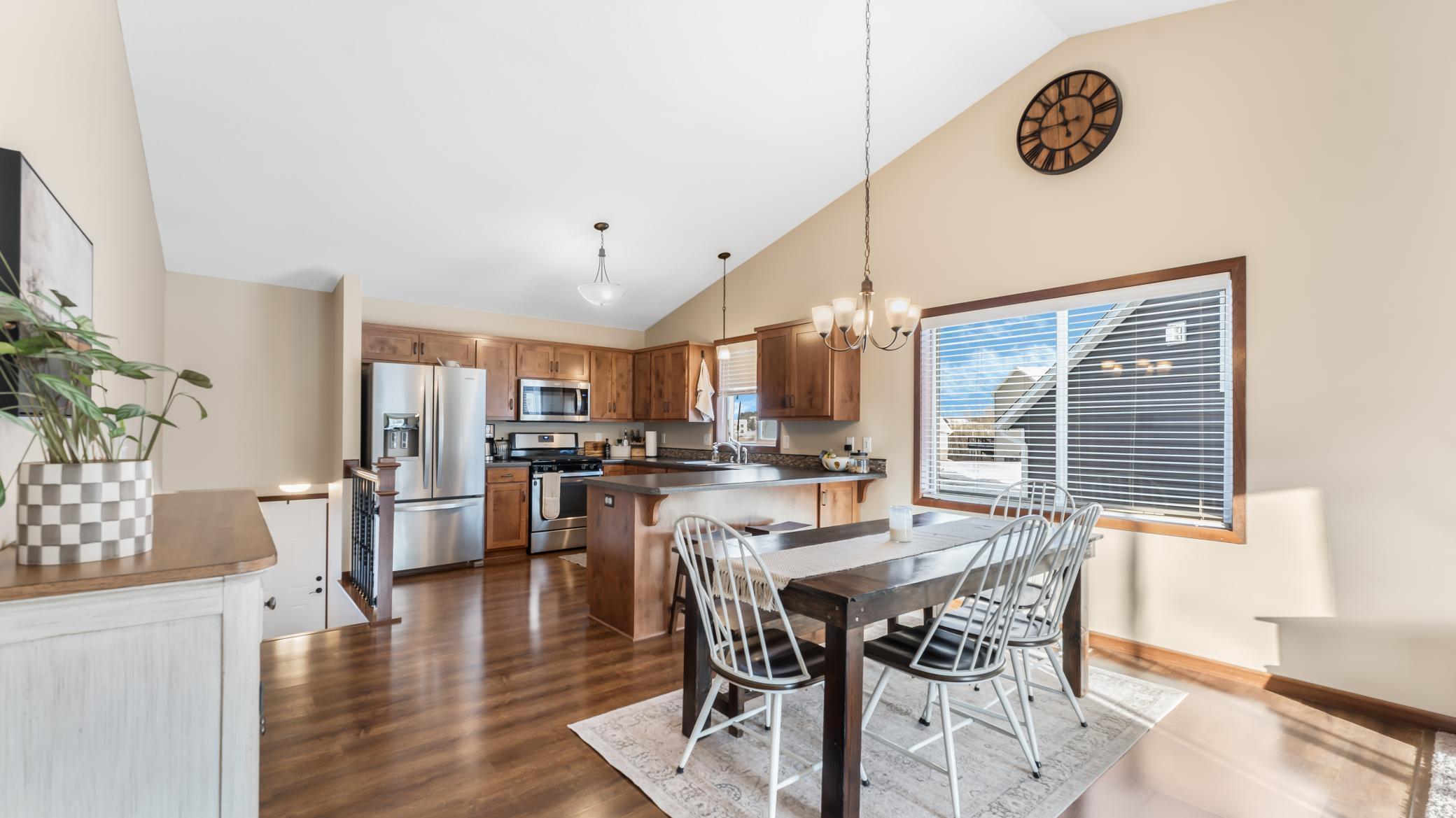 Kitchen and dining area with wood cabinets, stainless steel appliances, and a dark table beside a wide window.
