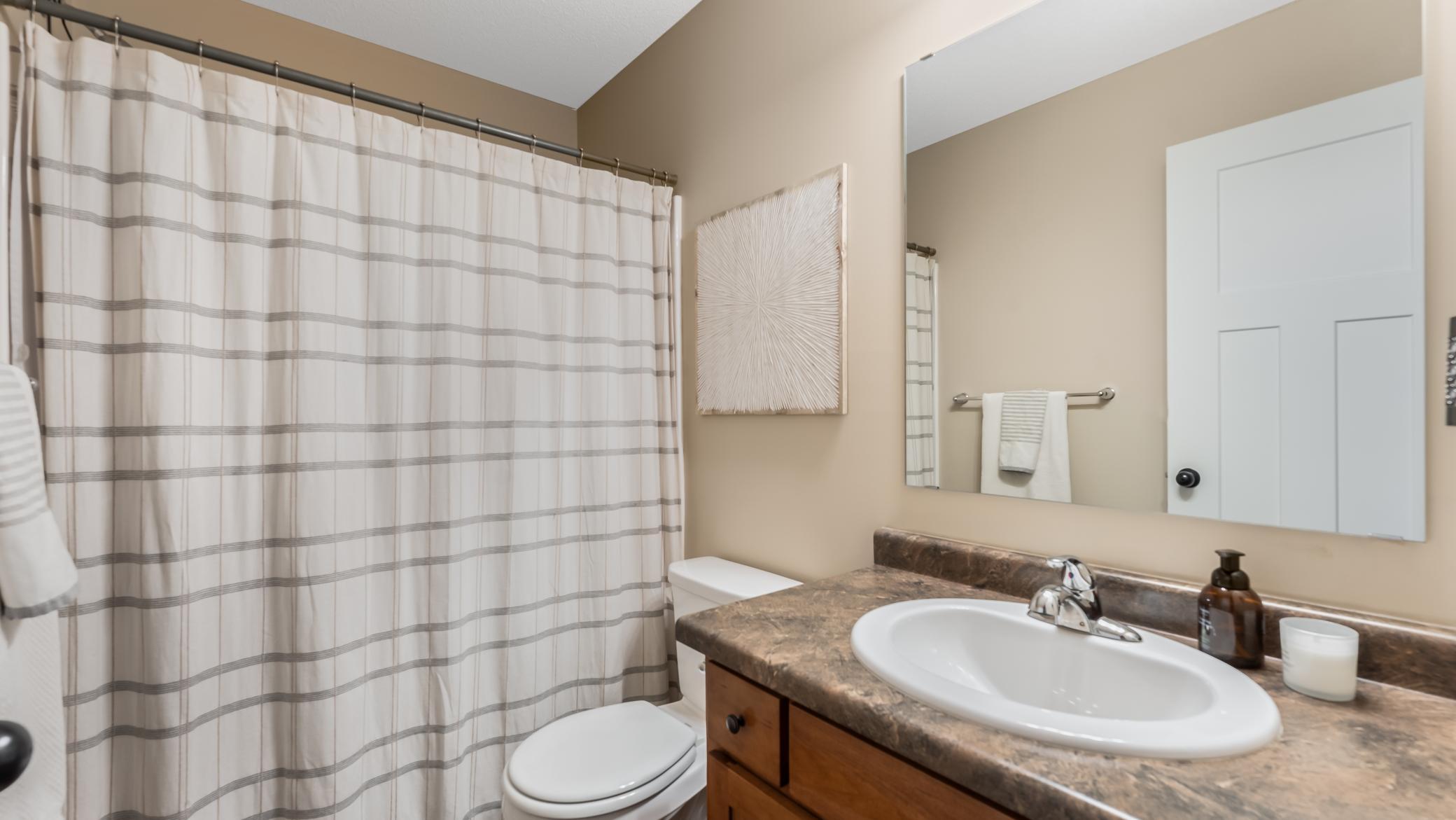 Bathroom with a striped shower curtain, toilet, and wood vanity with a white sink.