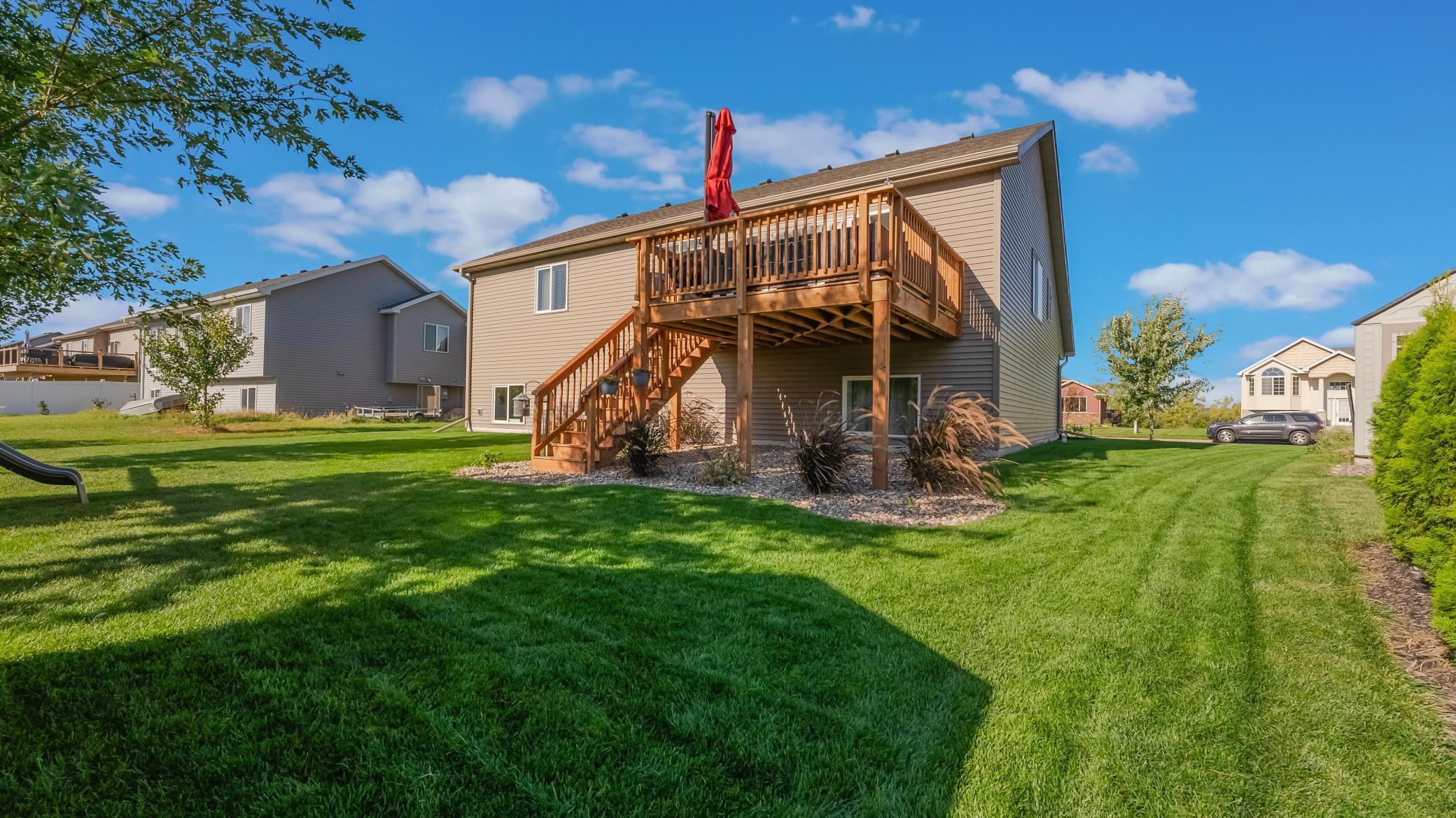 Home’s rear exterior with a raised wood deck and stairs overlooking a broad lawn.
