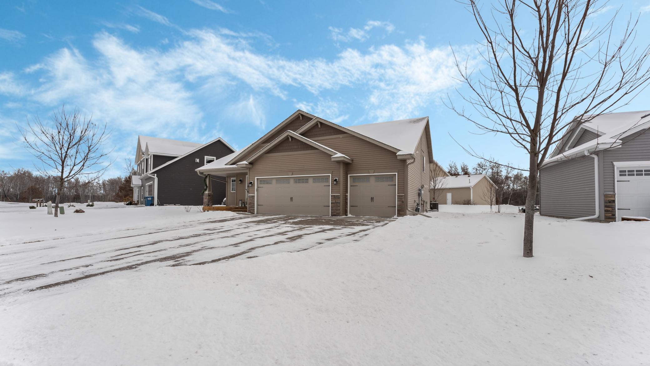 Brown-sided home with two garage doors and a snow-covered driveway.