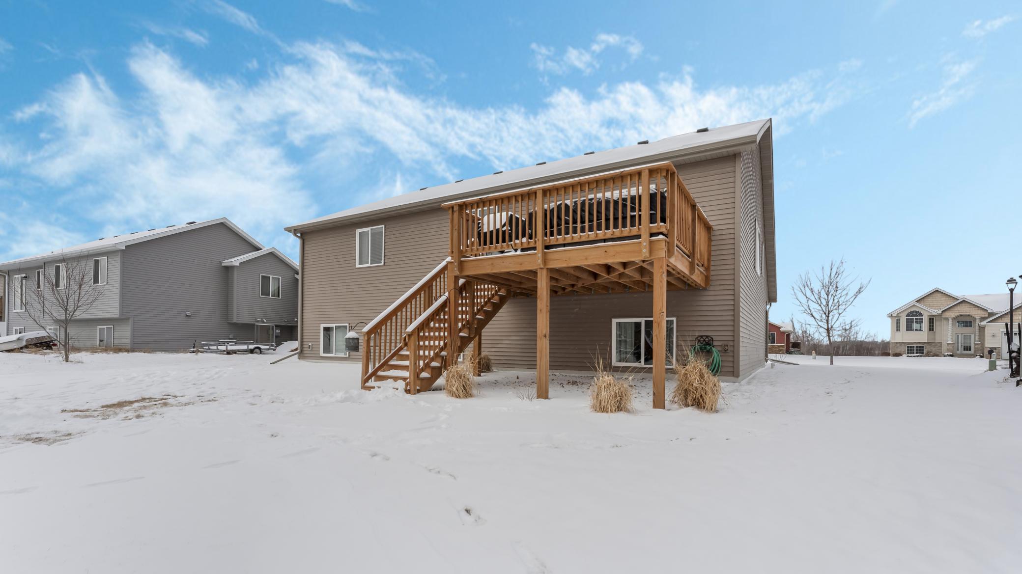 Home’s rear exterior with a raised wooden deck and stairs surrounded by snow.