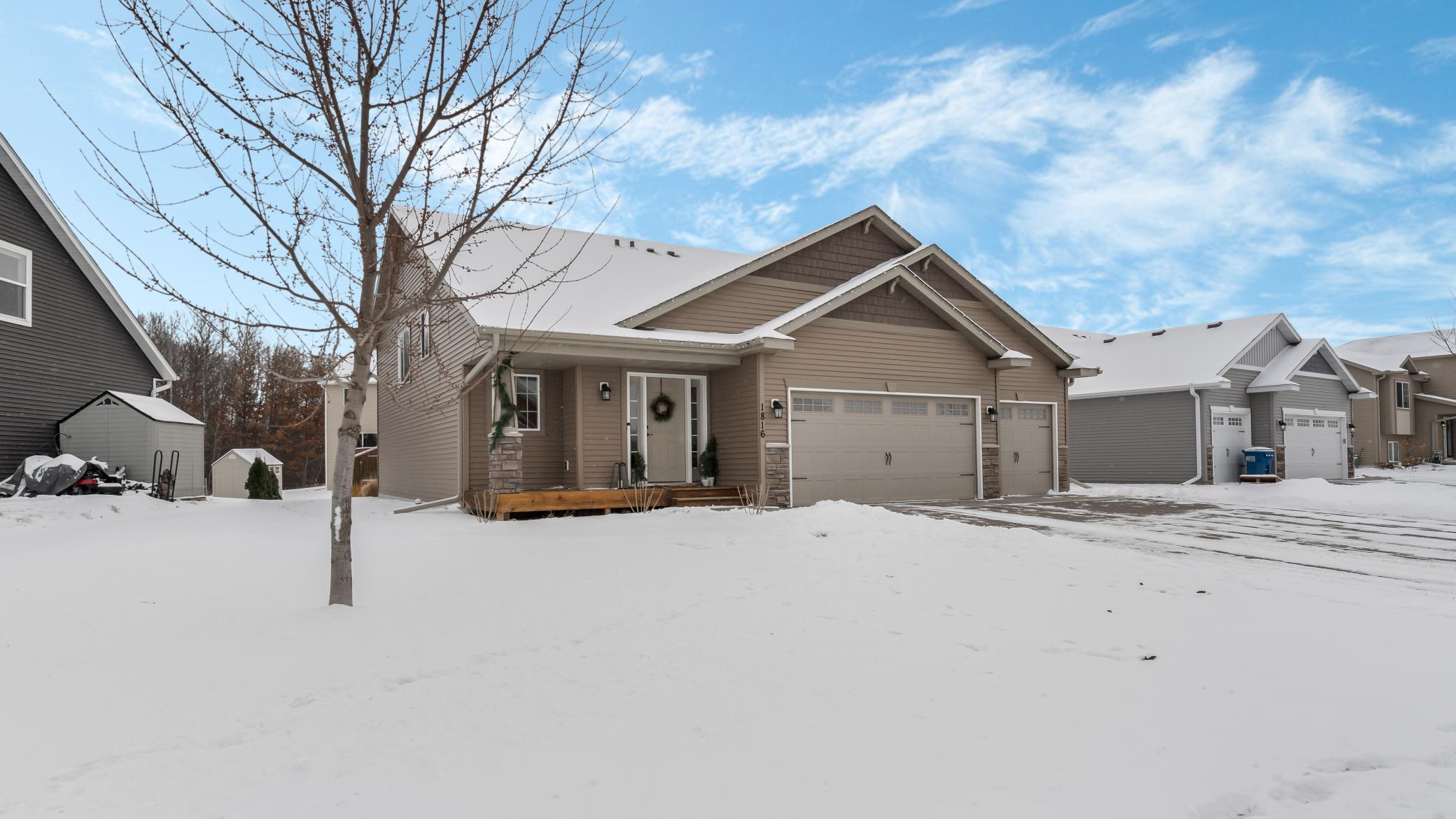 Taupe home with a covered porch and three-car garage, photographed in a snowy neighborhood.