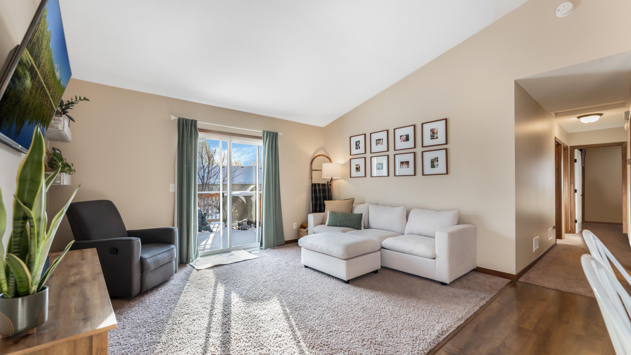 Living room with a white sectional, dark armchair, and sliding glass door opening to a deck.