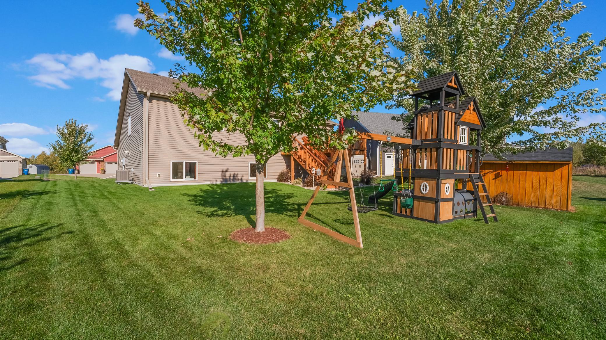 Backyard with a large wooden playset, swings, mature trees, and a spacious lawn.