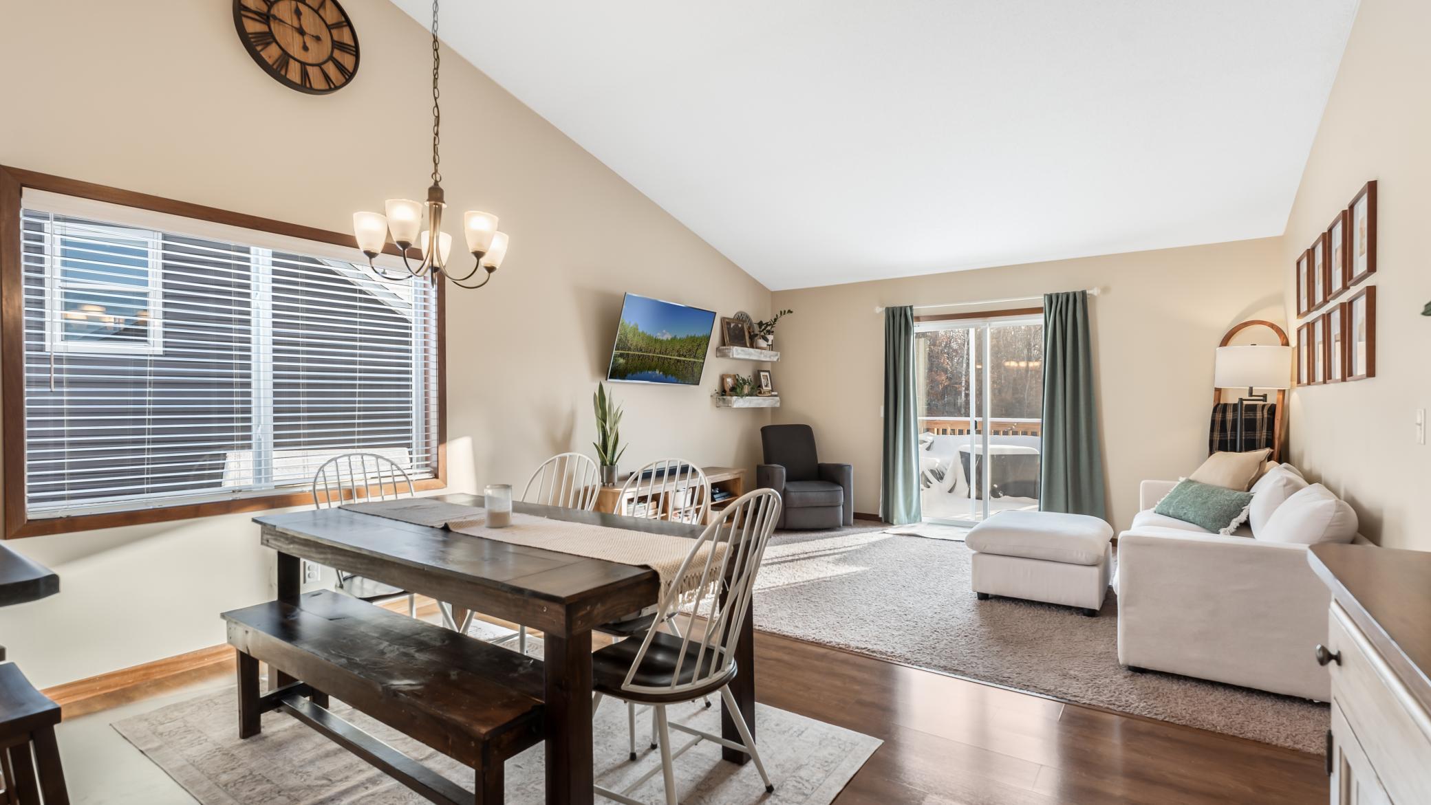 Open-plan dining and living room with a vaulted ceiling, dark wood dining table, and sliding glass doors to a deck.