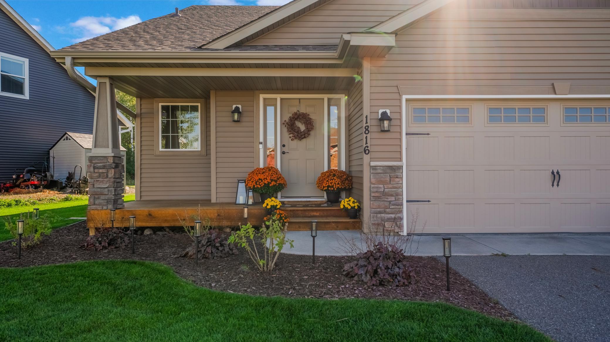 Home exterior with a covered porch, stone-based columns, attached garage, and autumn flowers.