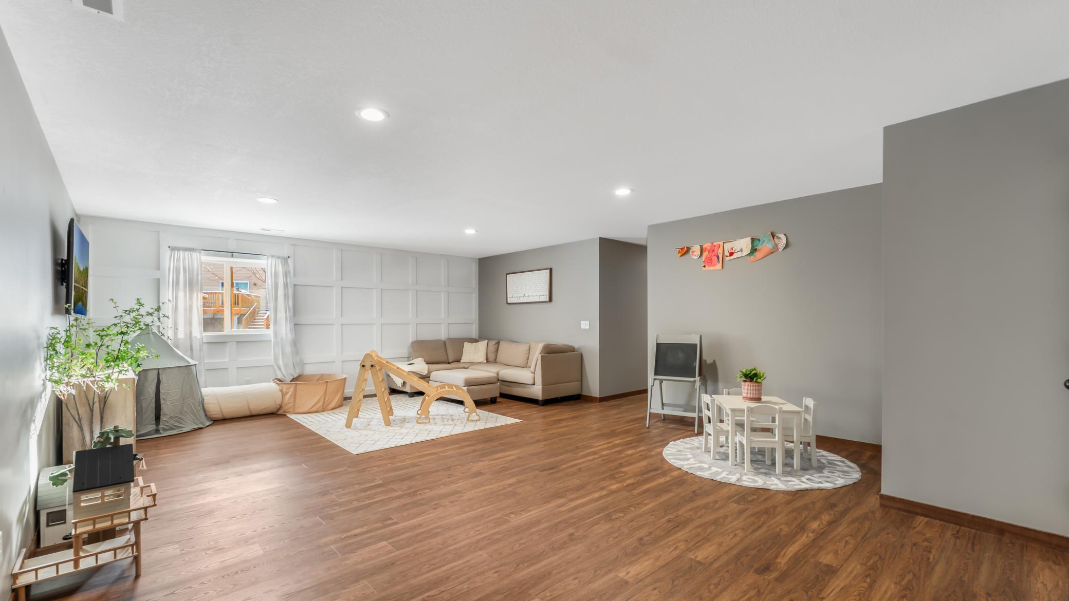 Living room with a beige sectional, wood floors, and a children’s play area.