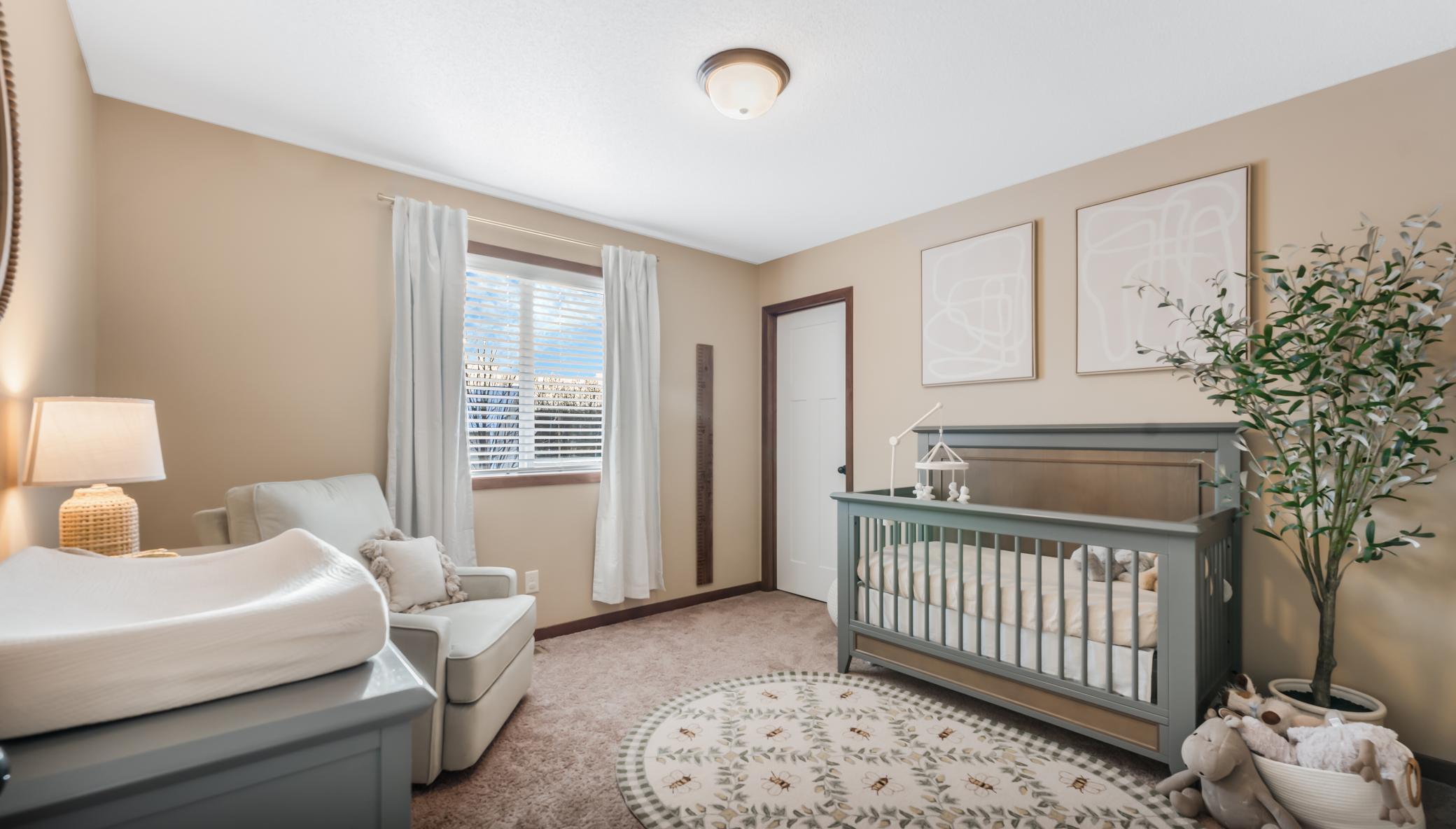 Nursery with a gray-green crib, matching changing table, and white armchair beside a curtained window.