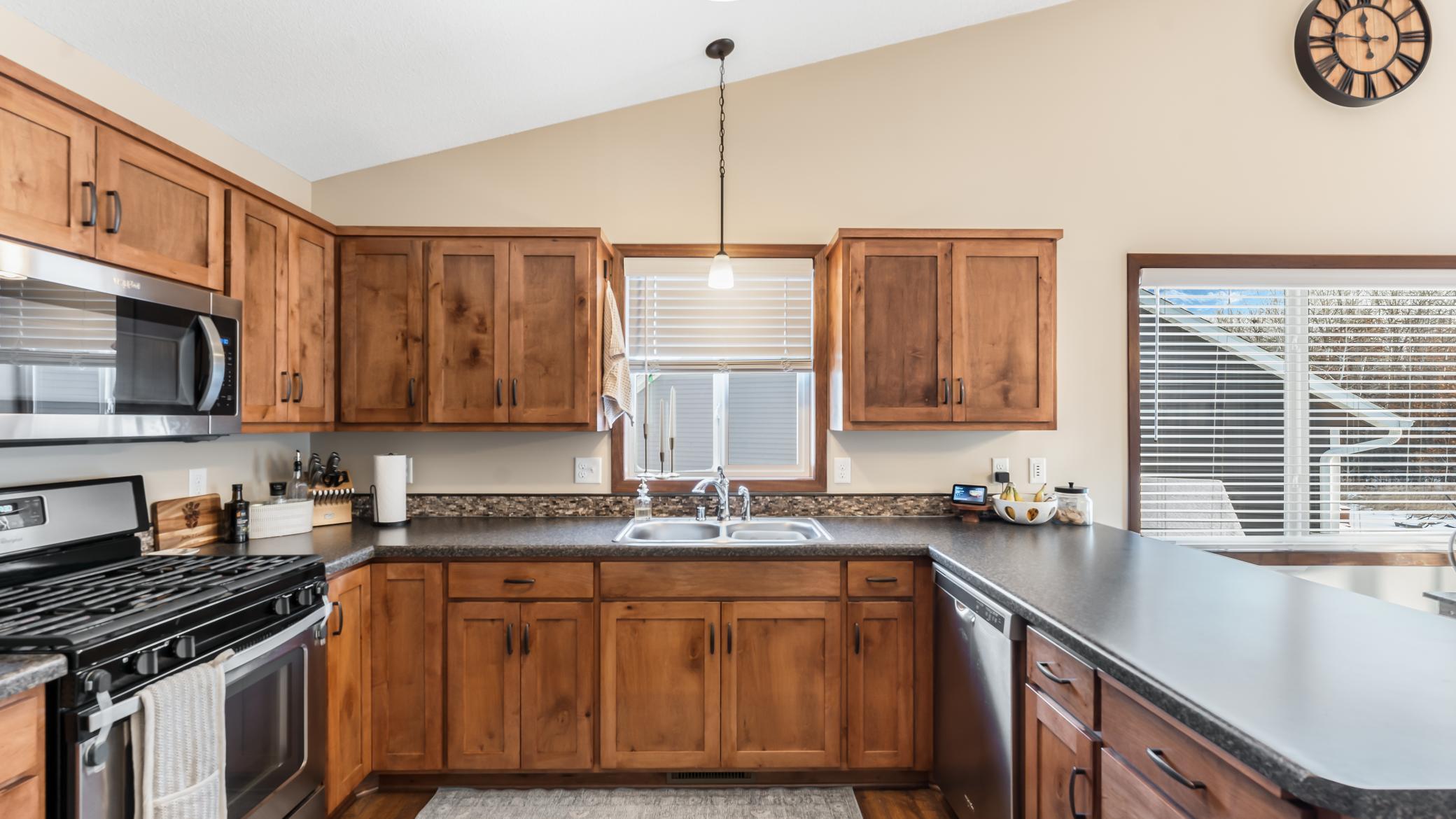 Kitchen with warm wood cabinets, dark counters, stainless steel appliances, and a sink beneath the window.
