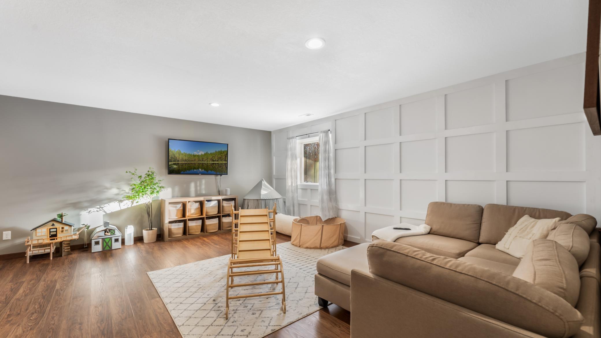 Family room with a beige sectional, white paneled wall, and children's play area.