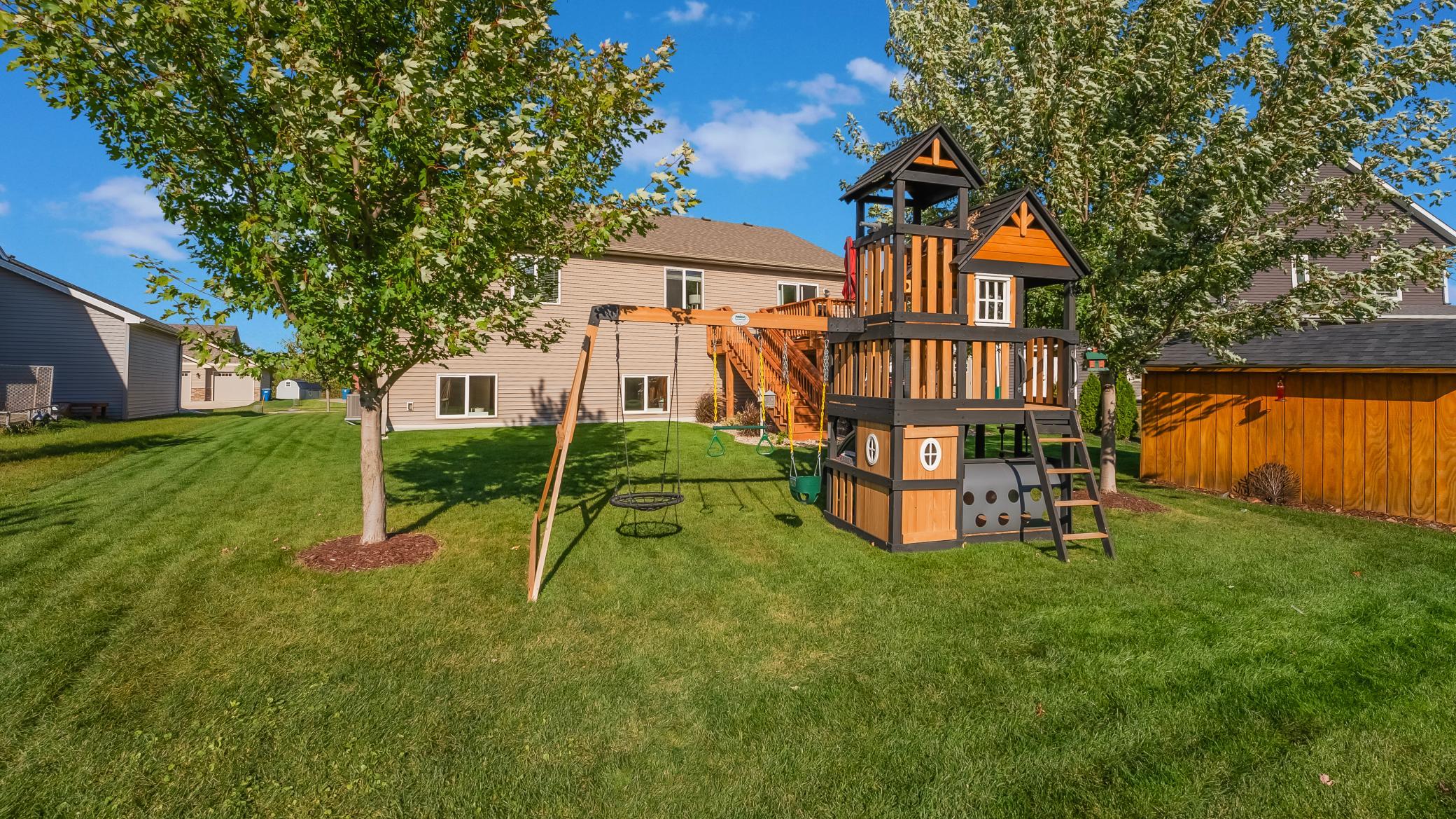 Backyard with a large wooden playset and swings on a broad green lawn.