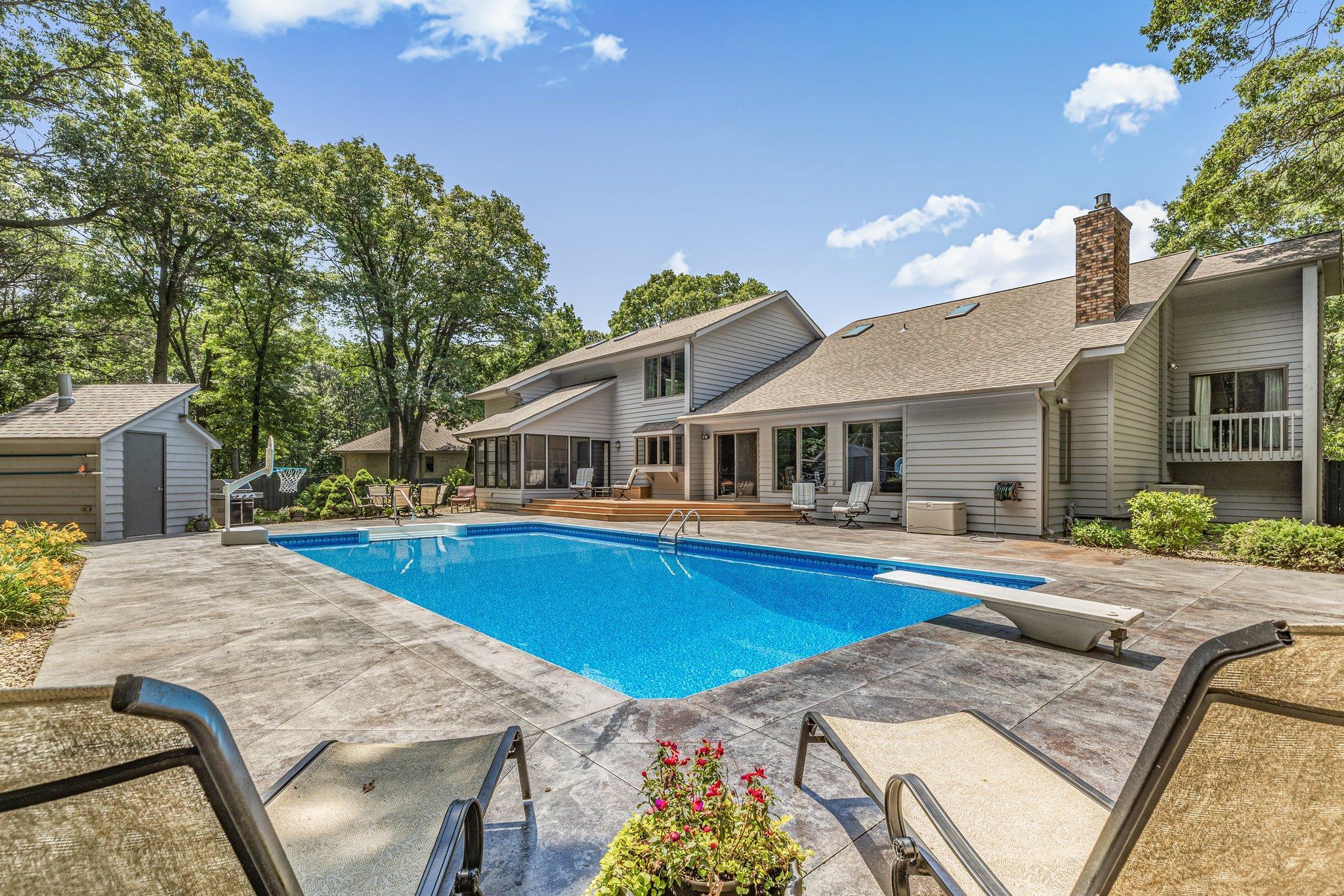 Backyard pool beside a gray home, with a stone patio and lounge chairs.