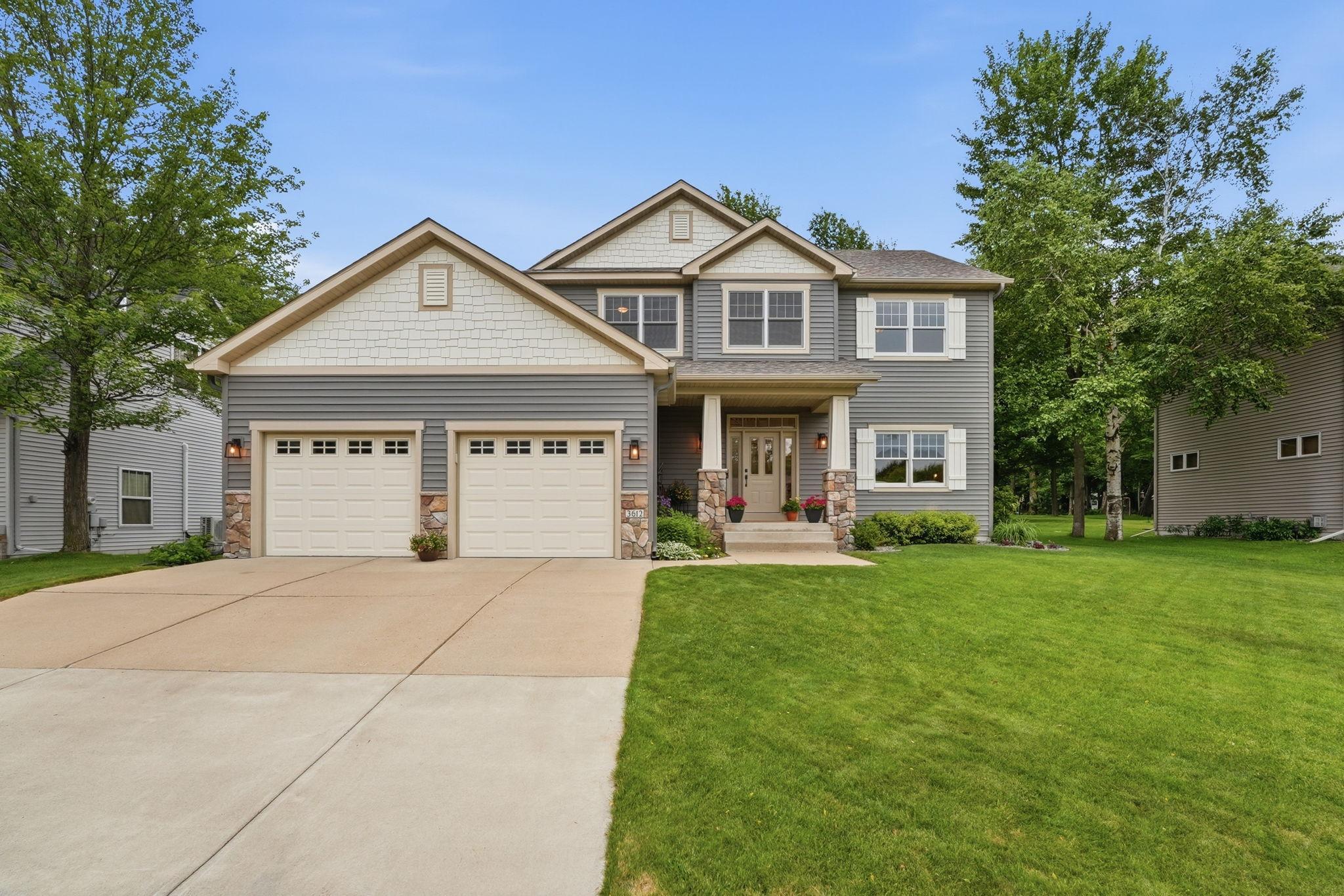 Gray two-story home with a double garage, stone porch accents, and a broad concrete driveway.