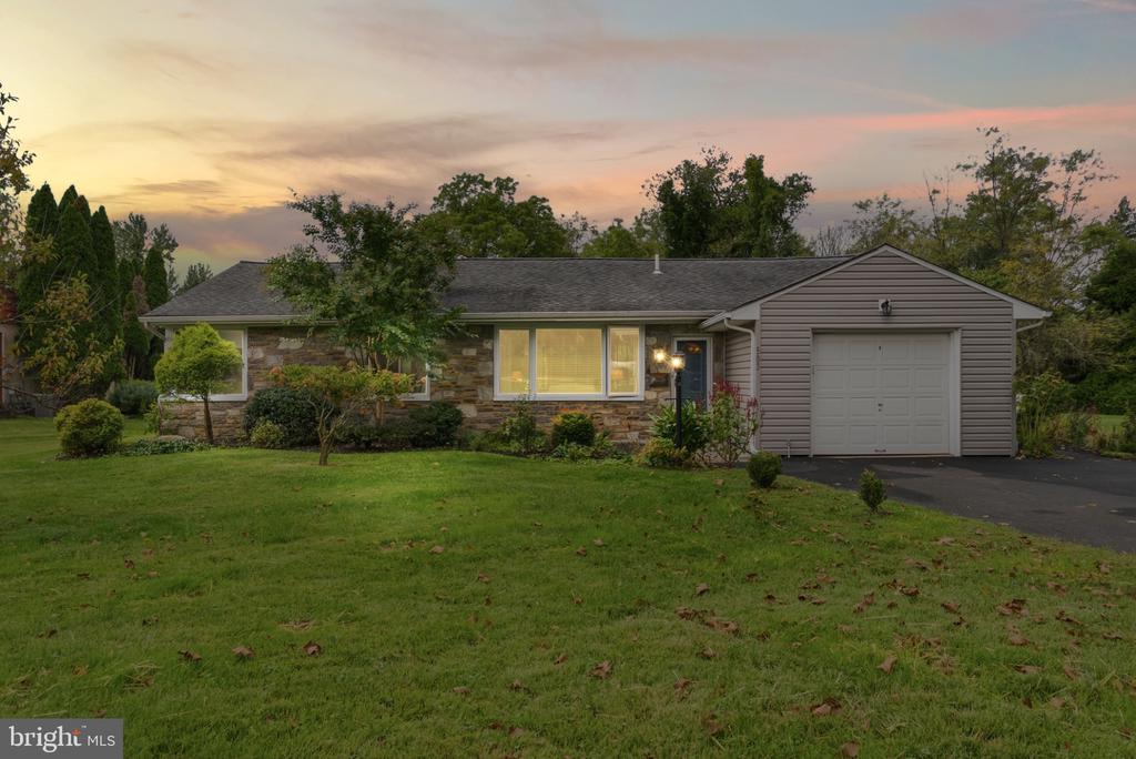 Single-story stone-and-siding home with an attached garage, broad lawn, and pastel sunset sky.